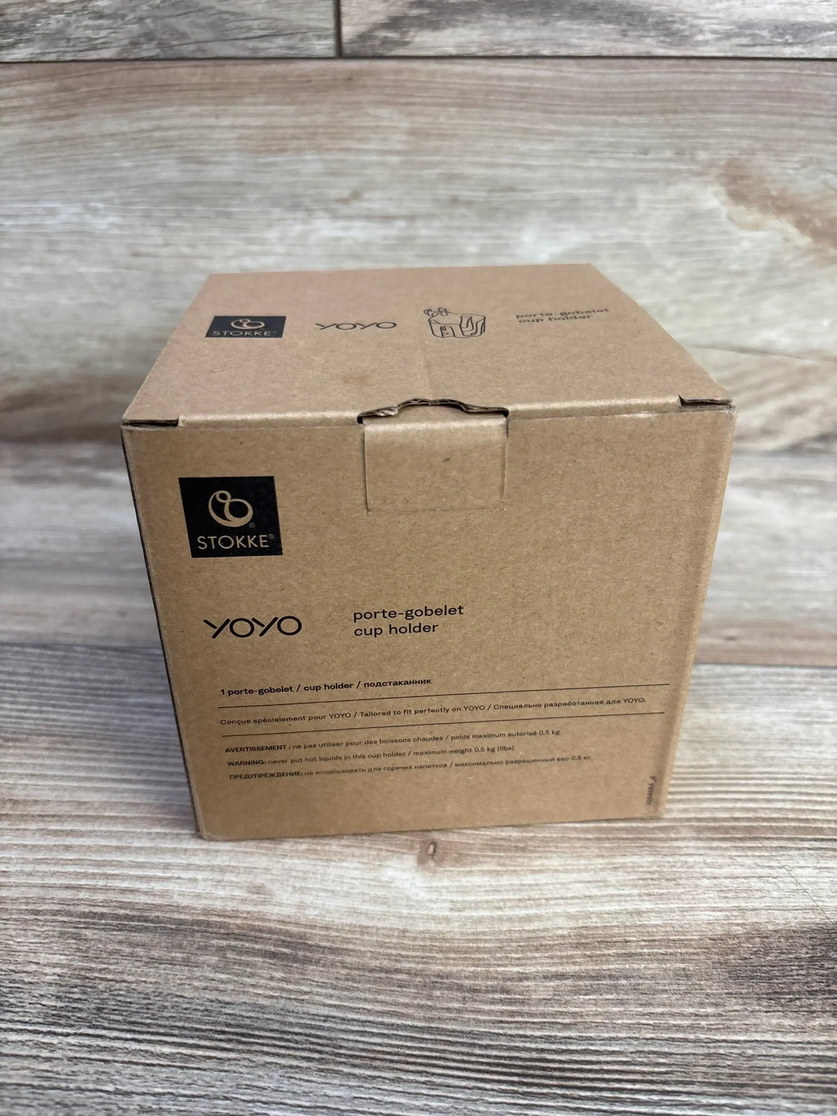 Front view of boxed Stokke YOYO stroller cup holder (black) showing Stokke logo and product label on a wood surface