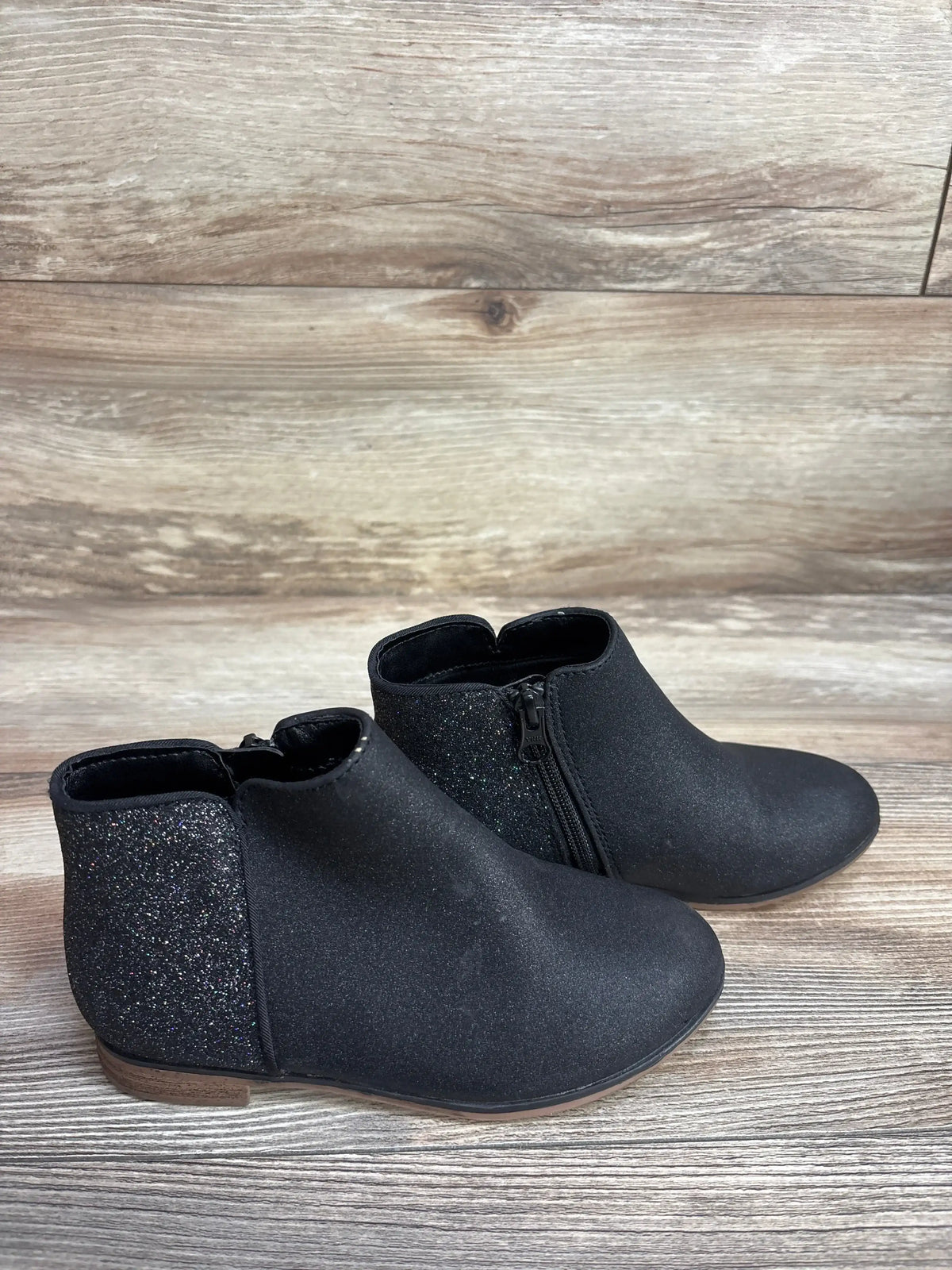 Black toddler ankle boots with side zipper and glitter heel panel on wood background