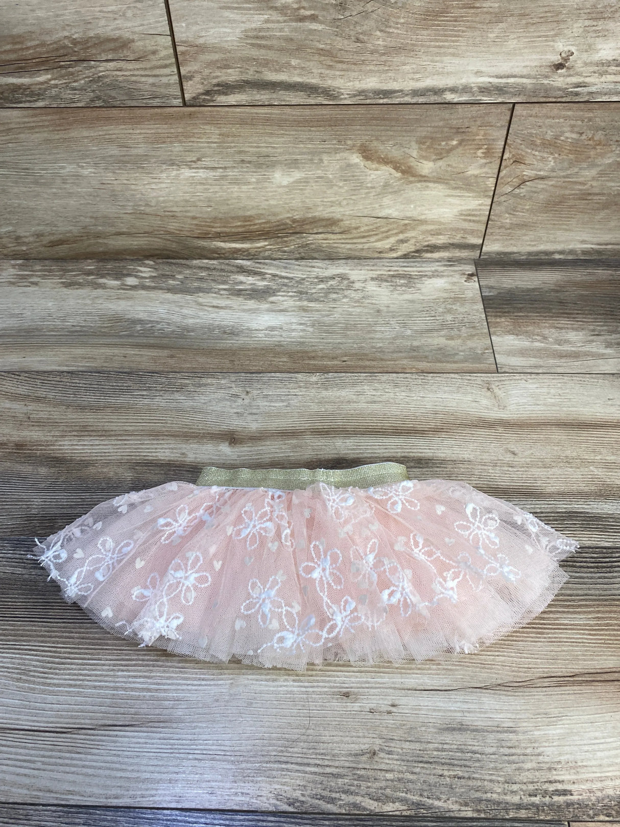 Flat lay of pink embroidered tulle baby skirt showcasing white floral embroidery and gold elastic waistband on wood background