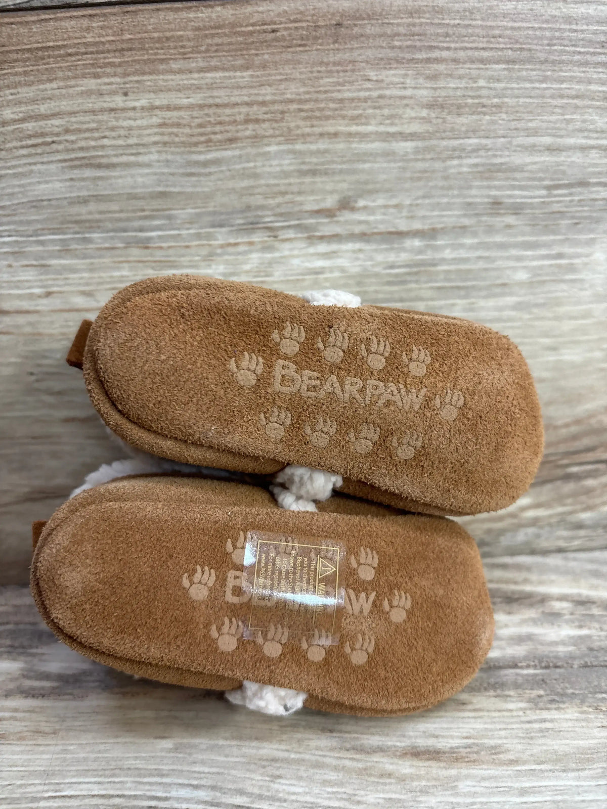 Bearpaw brown toddler slippers with soft suede soles and paw print traction on rustic wood surface