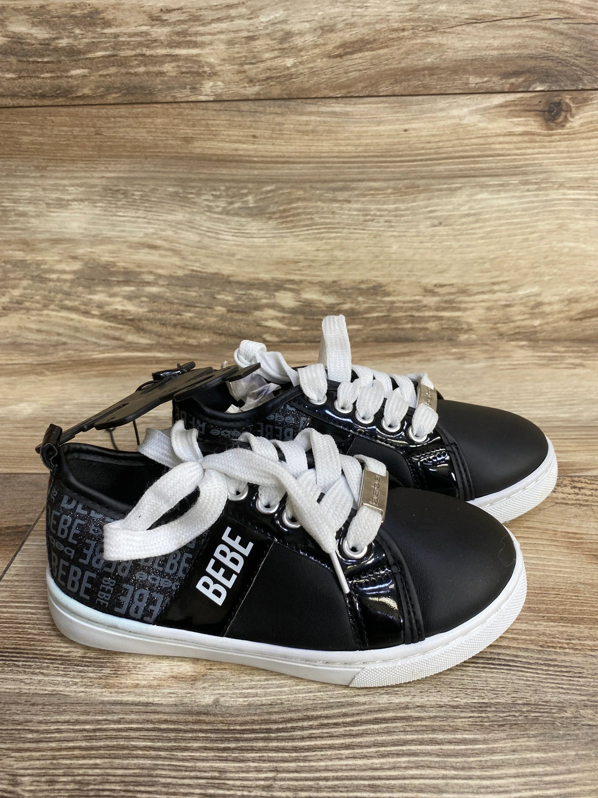 Side view of Bebe Chiara platform kids sneakers in black showcasing white laces, BEBE logo and metal lace tag on wood background