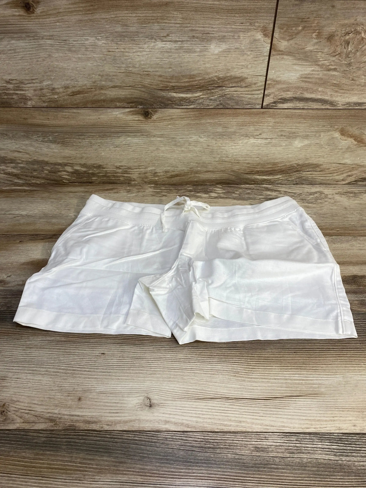 Front flat lay of white Gap maternity linen-cotton shorts, size large, showing elastic drawstring waist and cuffed hem on wood