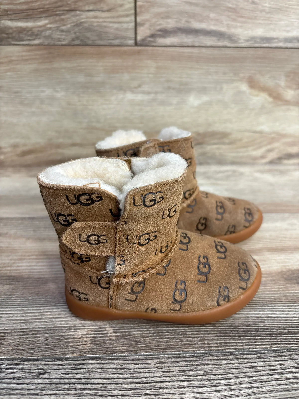 Pair of brown UGG toddler boots with shearling lining and logo print on wooden surface