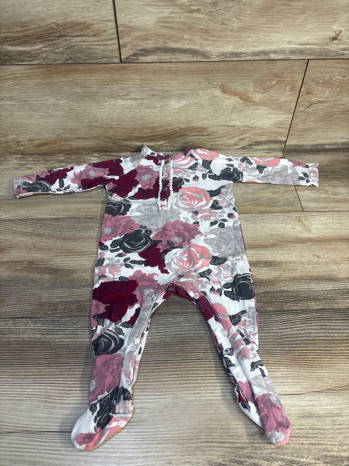 Floral baby onesie with pink, red, and black roses on white, laid on wood floor