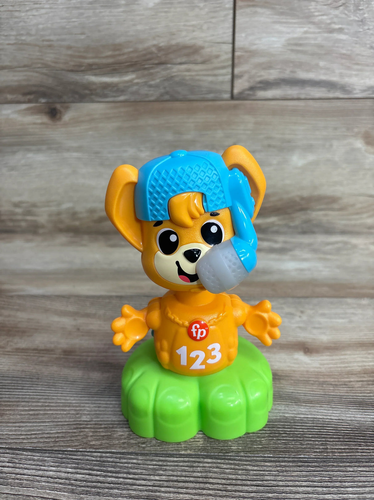 Front view of Fisher Price Link Squad Opposites fox toy showcasing orange fox in blue cap with 123 shirt on green base with wood plank background