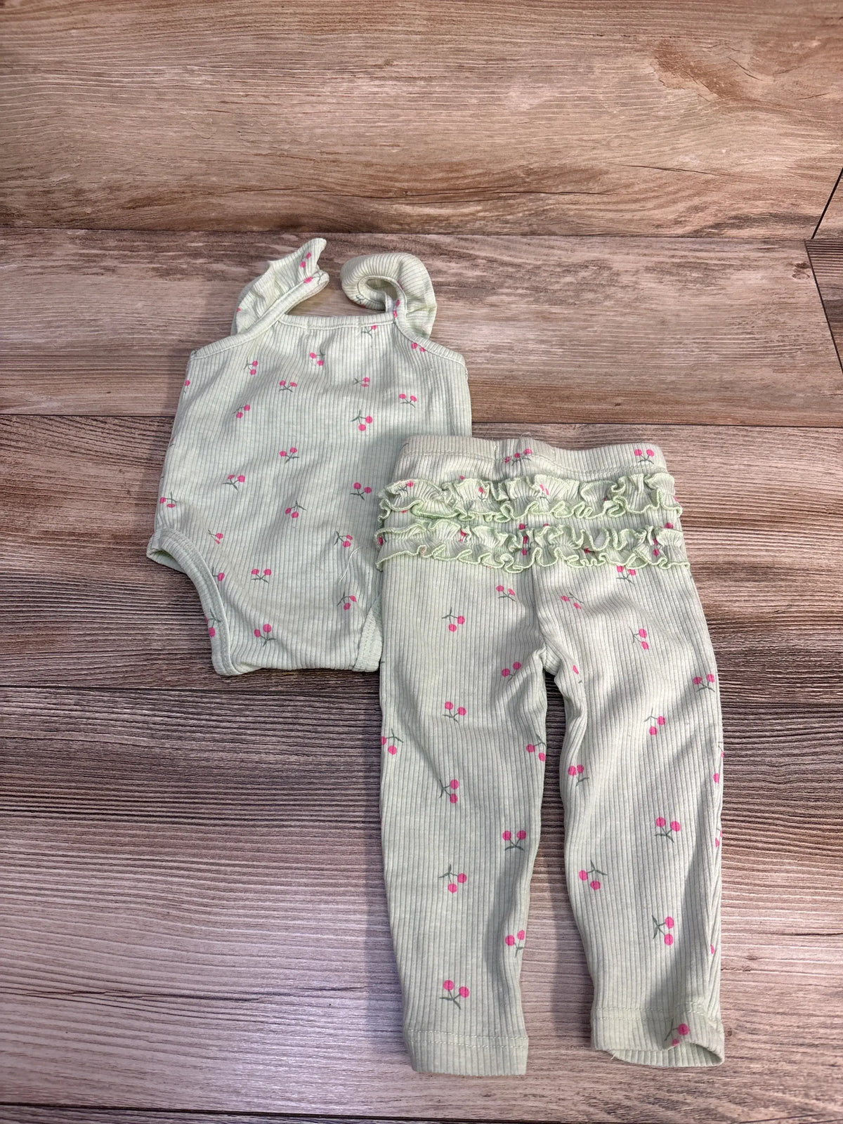 Overhead view of Btween baby two-piece ribbed tank bodysuit and pants set in green with pink cherry print on wood