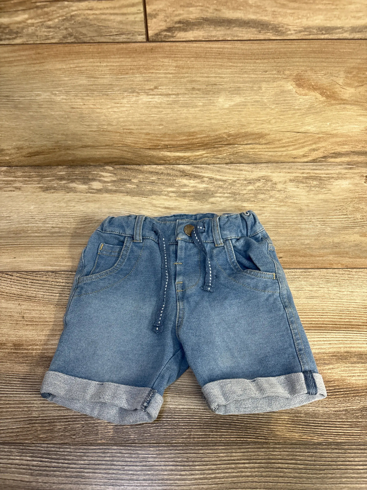Front view of Fox denim drawstring shorts showcasing blue denim, adjustable drawstring, pockets, and cuffed hems on a wood background