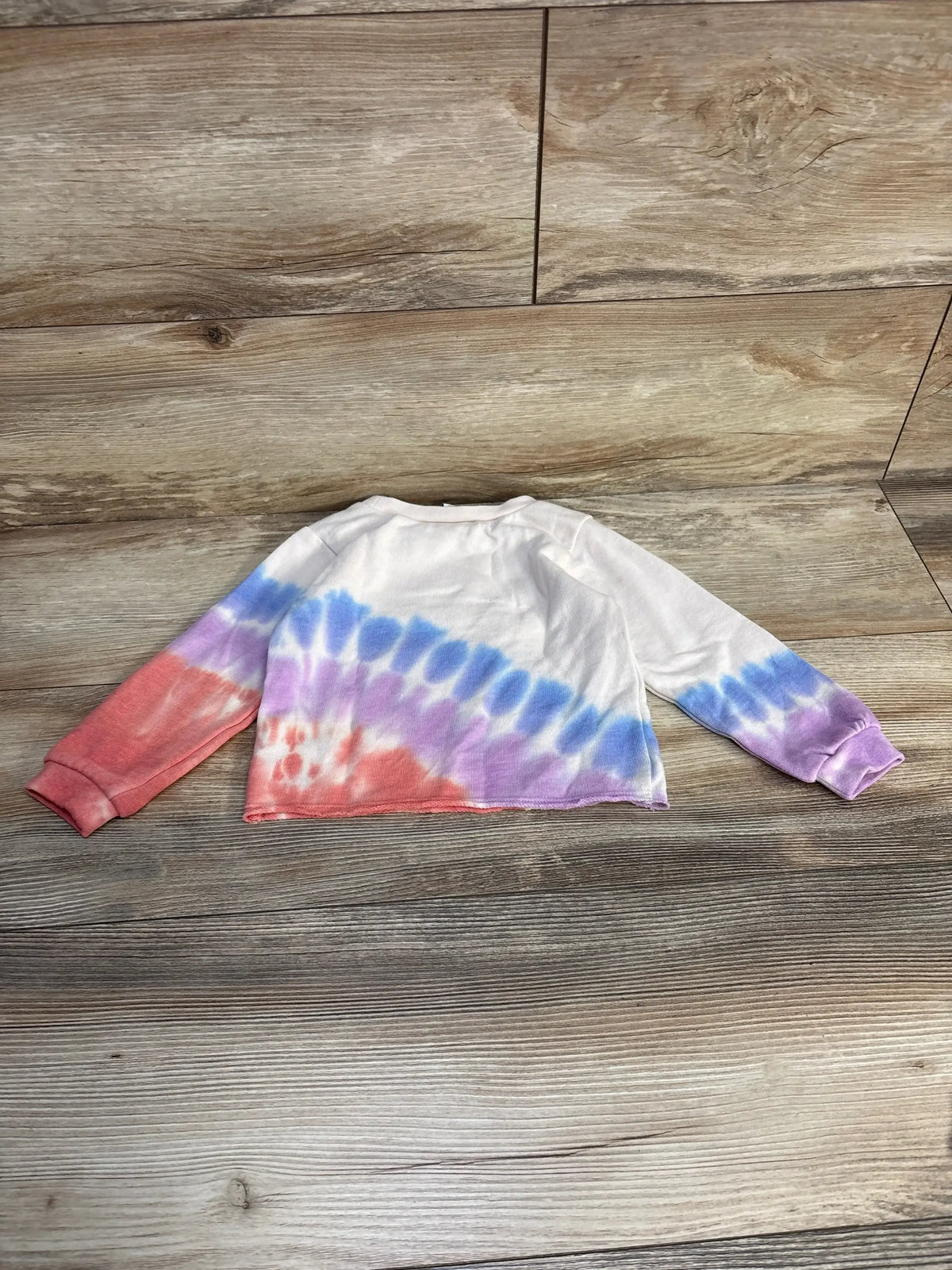 Kids long sleeve tie-dye shirt in red, purple, and blue on wood background