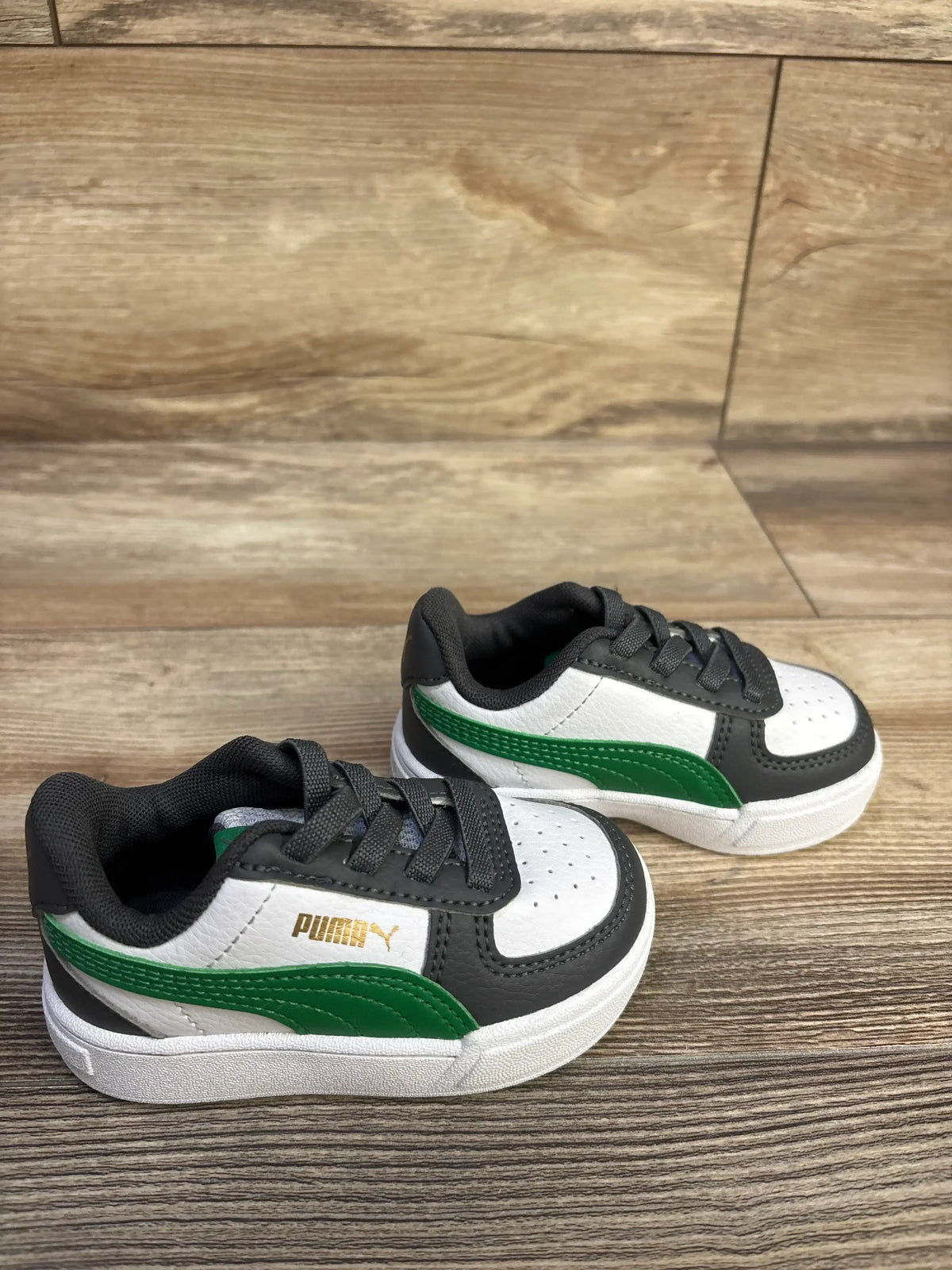 Angled side view of Puma Caven 2.0 toddler sneaker showing green Puma formstrip, gray trim, lace-up front, and gold Puma logo on wood floor