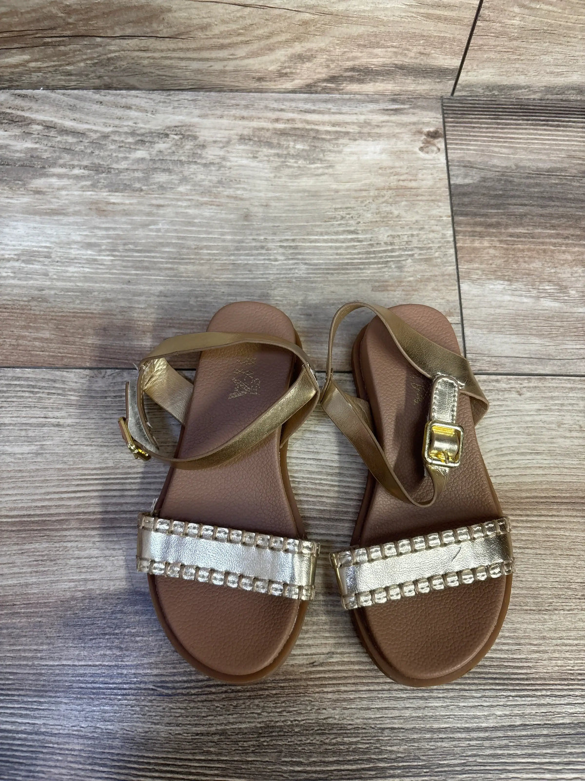 Top view of MIA Peyton toddler sandal size 8C in gold showcasing beaded front strap and adjustable ankle buckle on wood floor