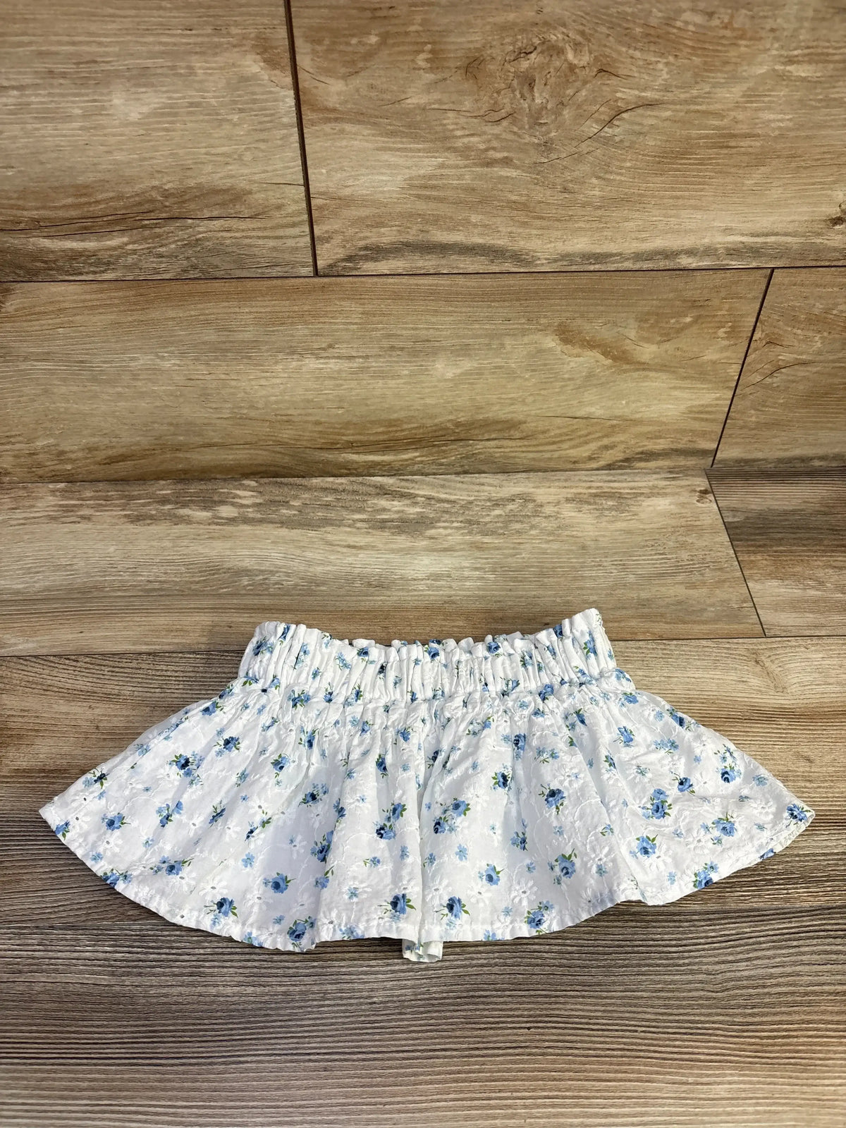 Flat lay of white Copper Key eyelet toddler skirt showing blue floral print and elastic gathered waistband on wood floor