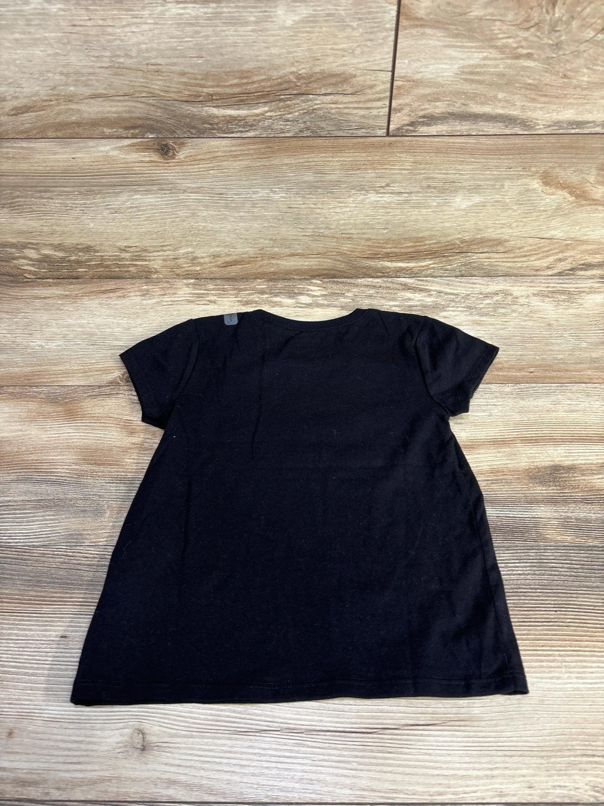 Back view flat lay of Children's Place black short-sleeve t-shirt showcasing plain back and short sleeves with light wood floor background
