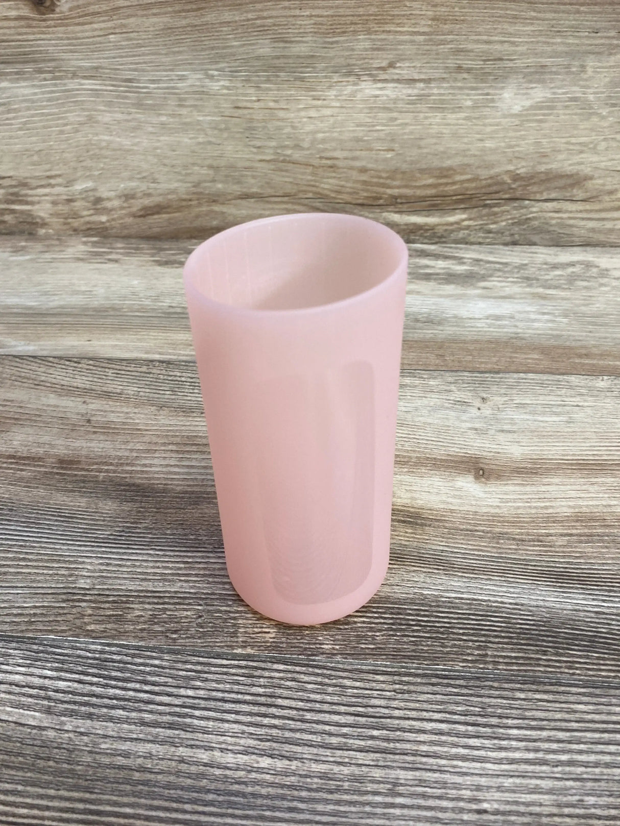 Angled view of Dr. Brown’s narrow pink 8 oz silicone bottle sleeve with inner ribs and smooth exterior on wood backdrop