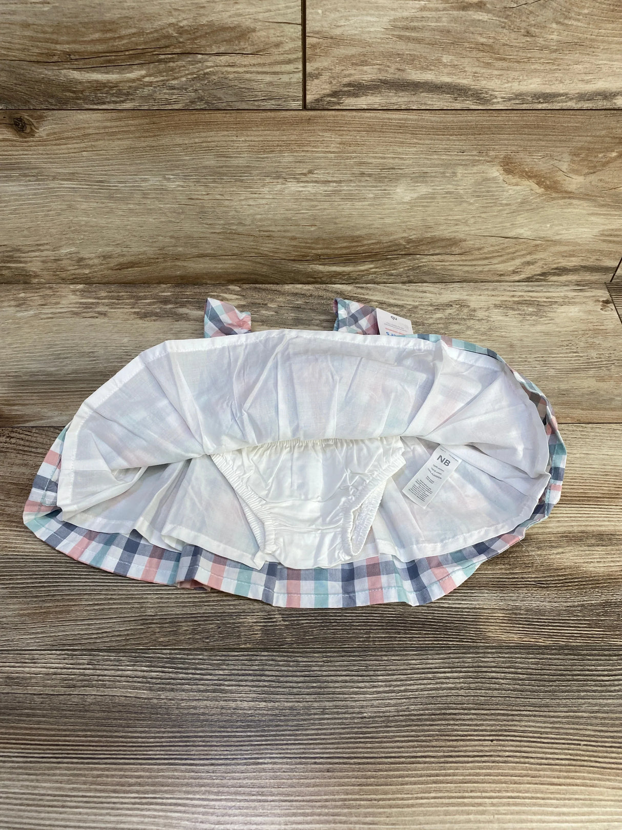 Top-down view of newborn plaid dress and matching bloomers in pastel checks with cotton lining on wood background