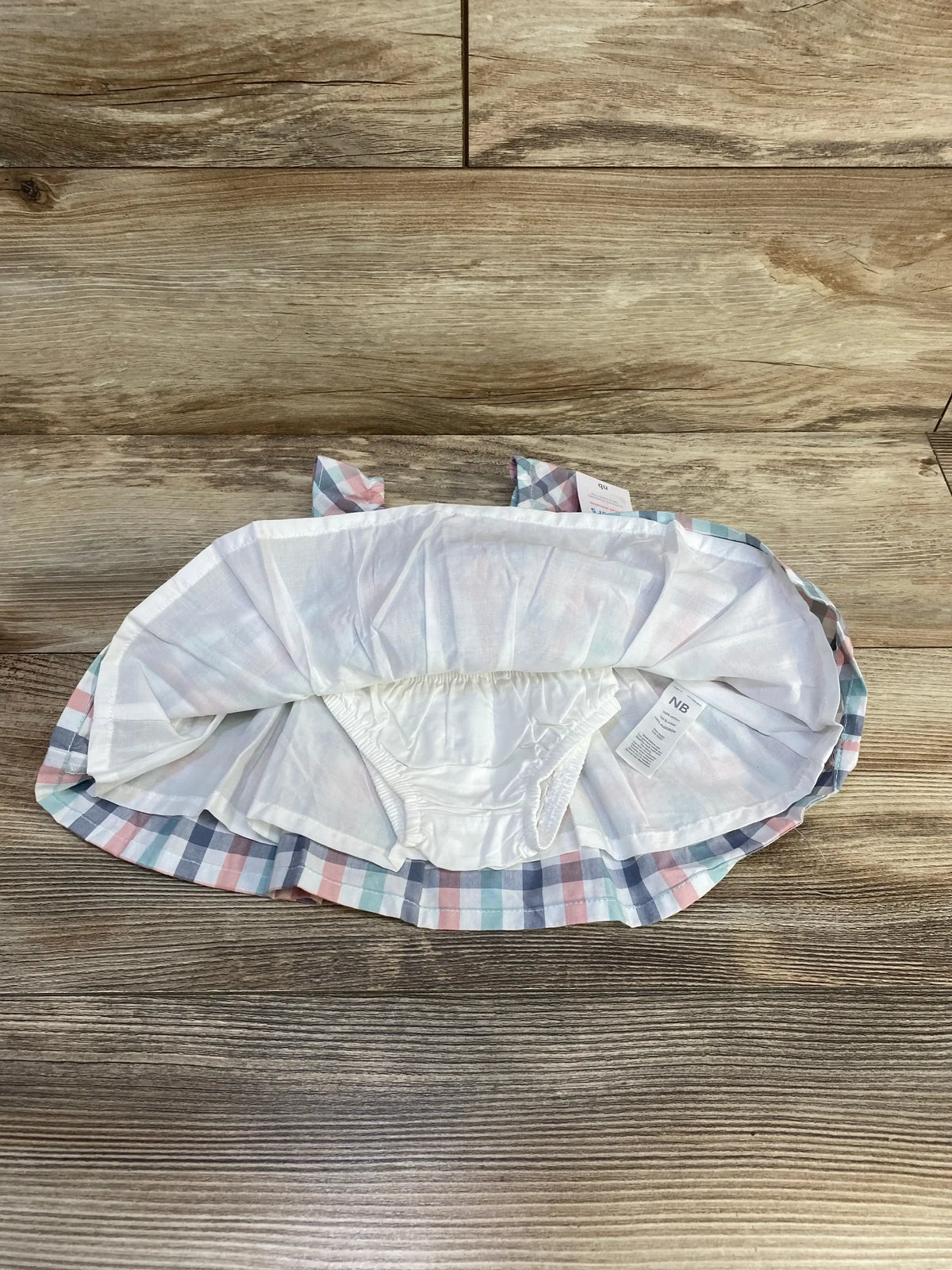 Top-down view of newborn plaid dress and matching bloomers in pastel checks with cotton lining on wood background