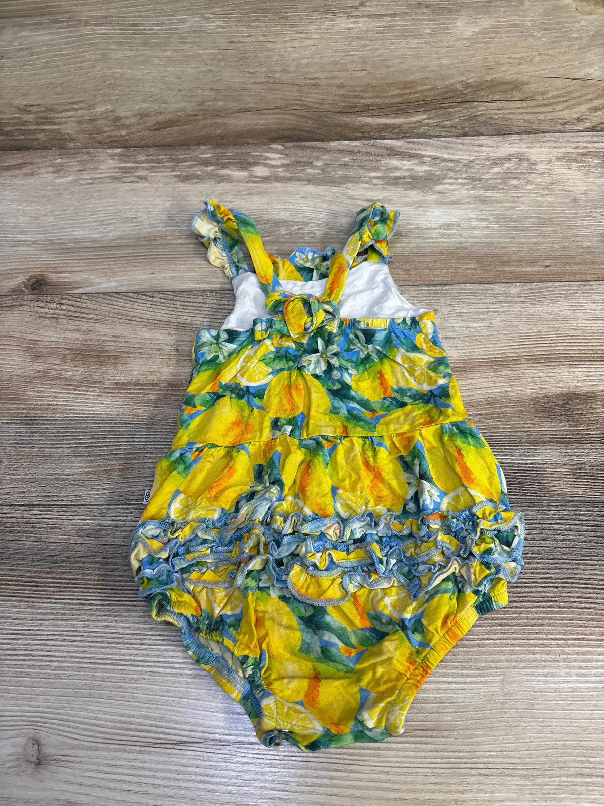 Front view of Little Bum Bums lemon print bamboo shortie romper with yellow lemon pattern and ruffled trim on wood grain