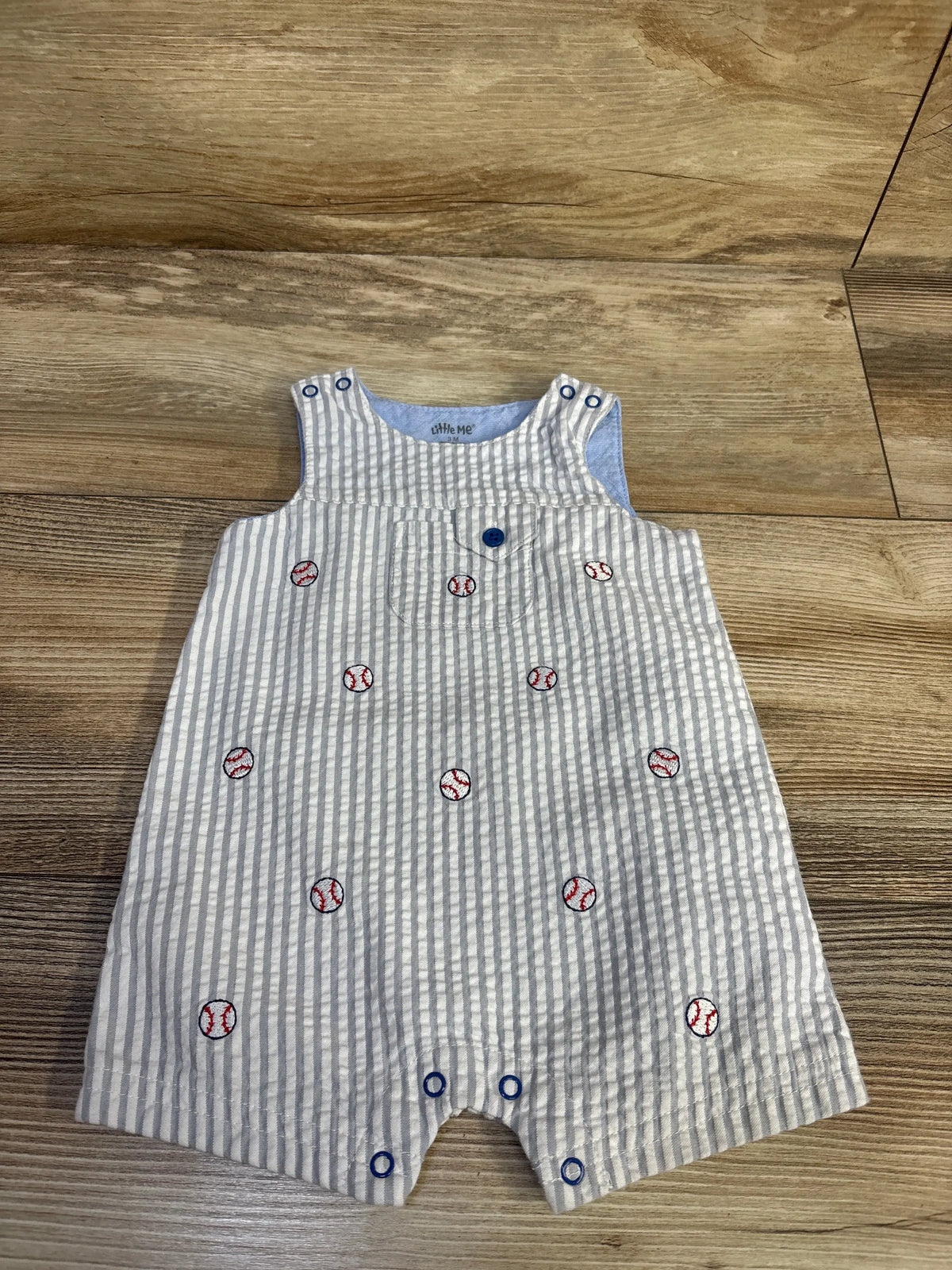 Front view of Little Me baseball seersucker romper showcasing white and gray stripes and baseball motifs on wood floor