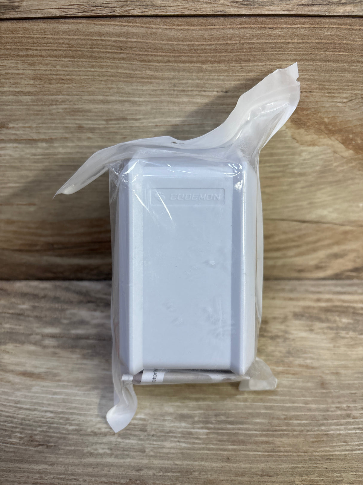 Front view of Eudemon white child safety outlet cover in sealed clear plastic packaging on wood background