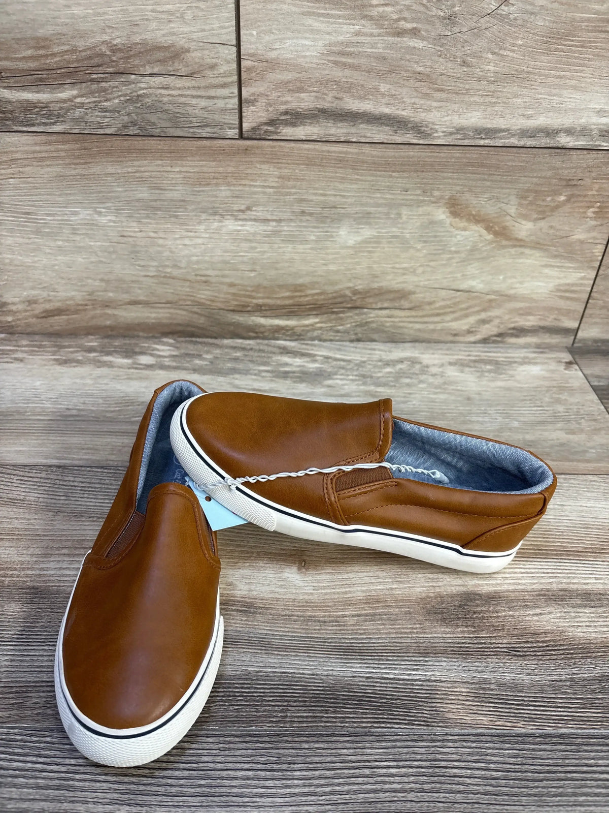 Three-quarter view of Cat & Jack Enzo slip-on sneakers, brown upper, elastic gussets, white sole on wood