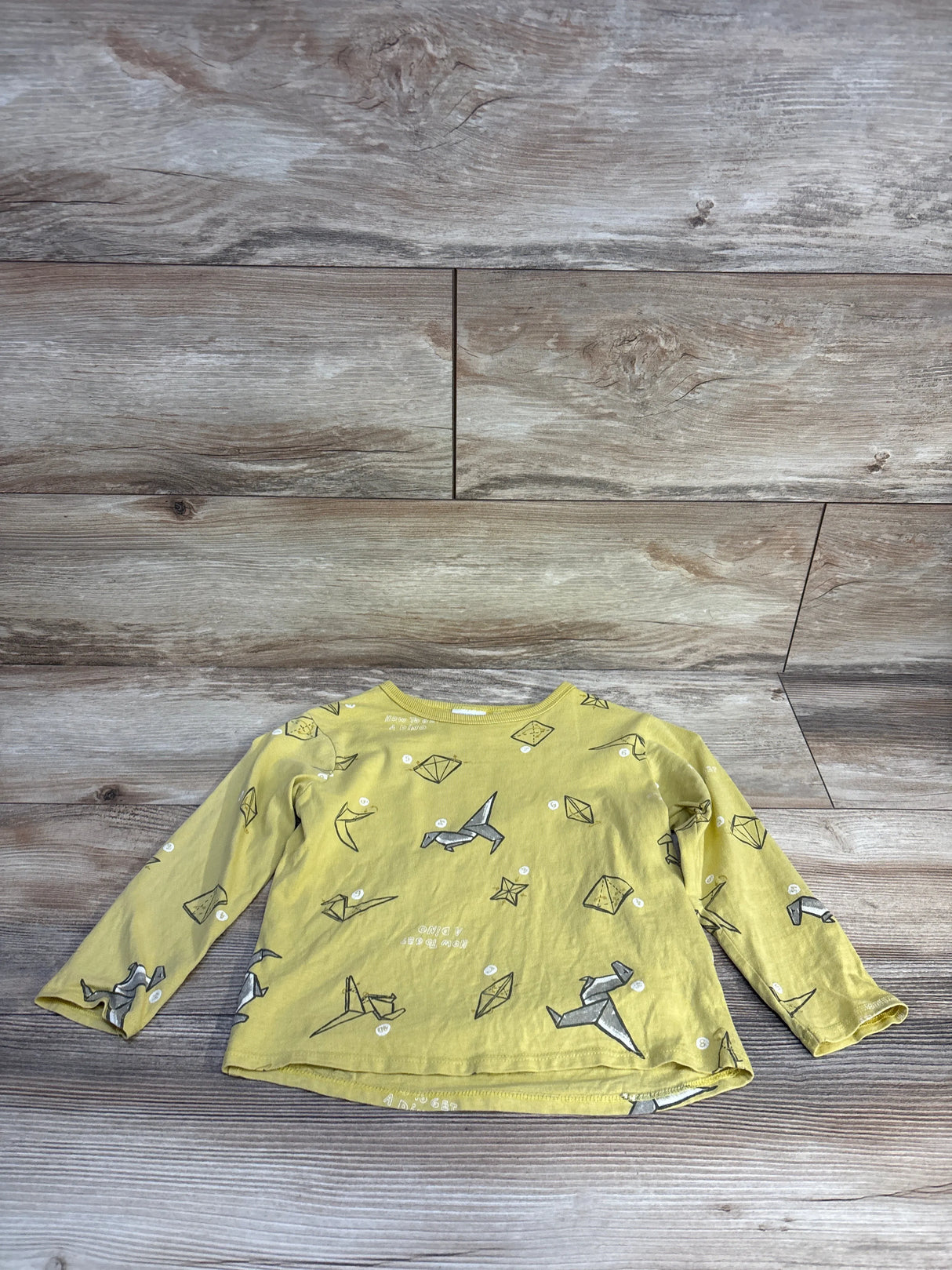 Yellow long sleeve kids shirt with origami animal and shape print, laid flat on wood