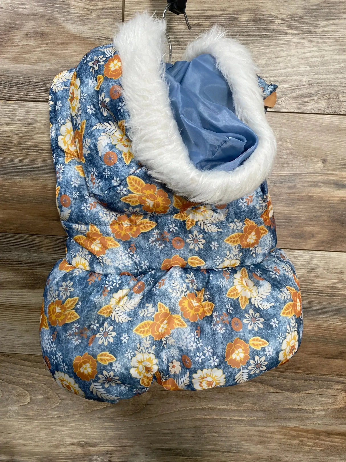 Front view of Little Lass floral hooded puffer vest in blue showing white faux fur trimmed hood and orange floral print on wood background