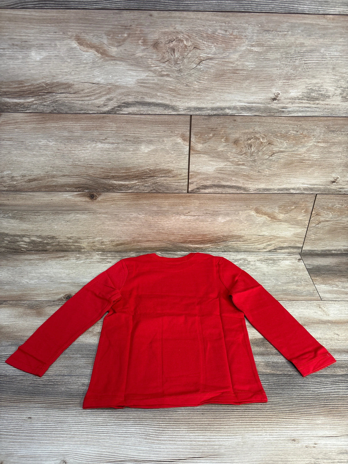 Red long-sleeve toddler shirt laid flat on wooden floor, children's apparel from resale store