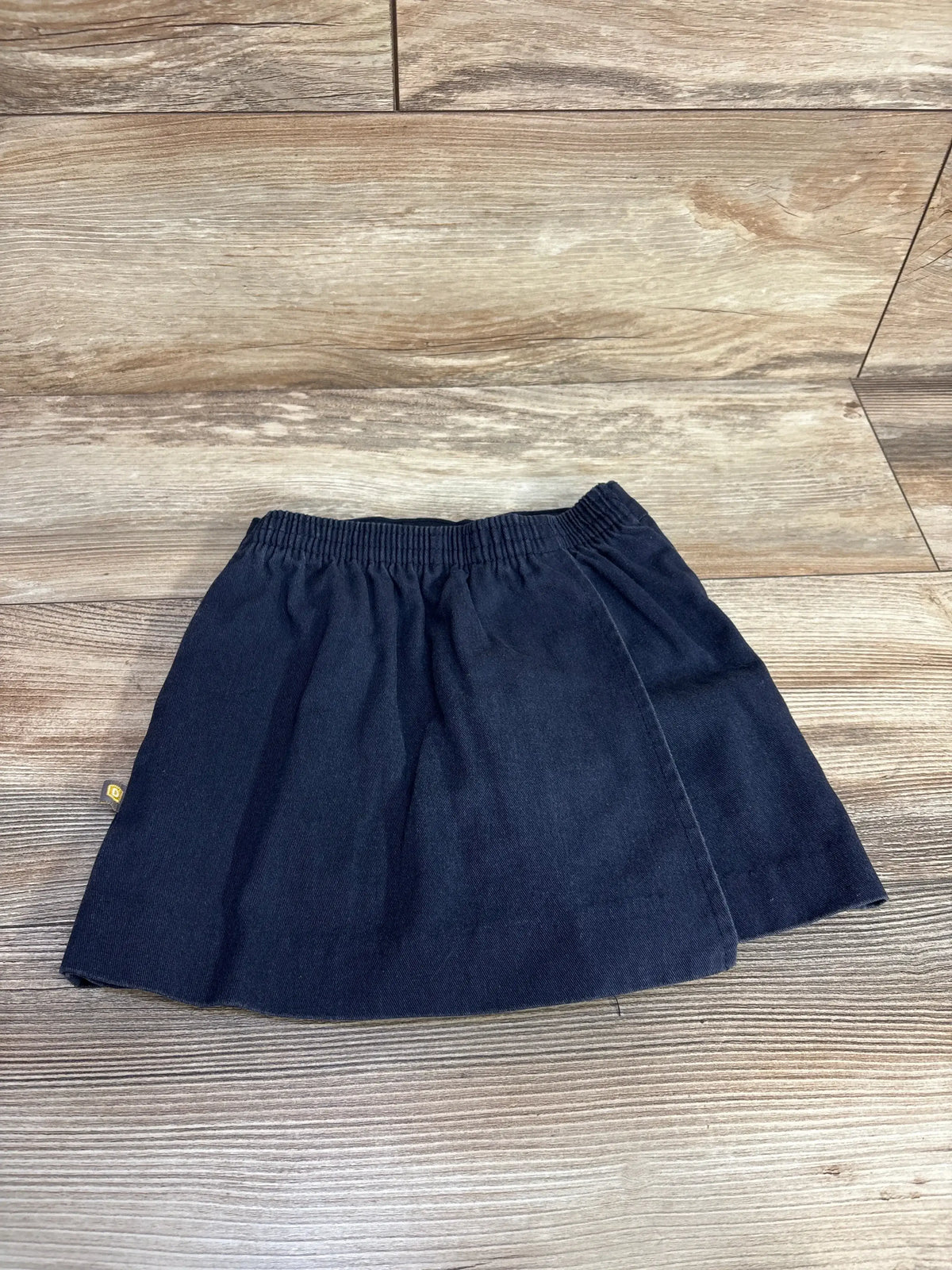 Front view of navy toddler skort (size 3T) showing elastic waistband and faux wrap front on wood floor background