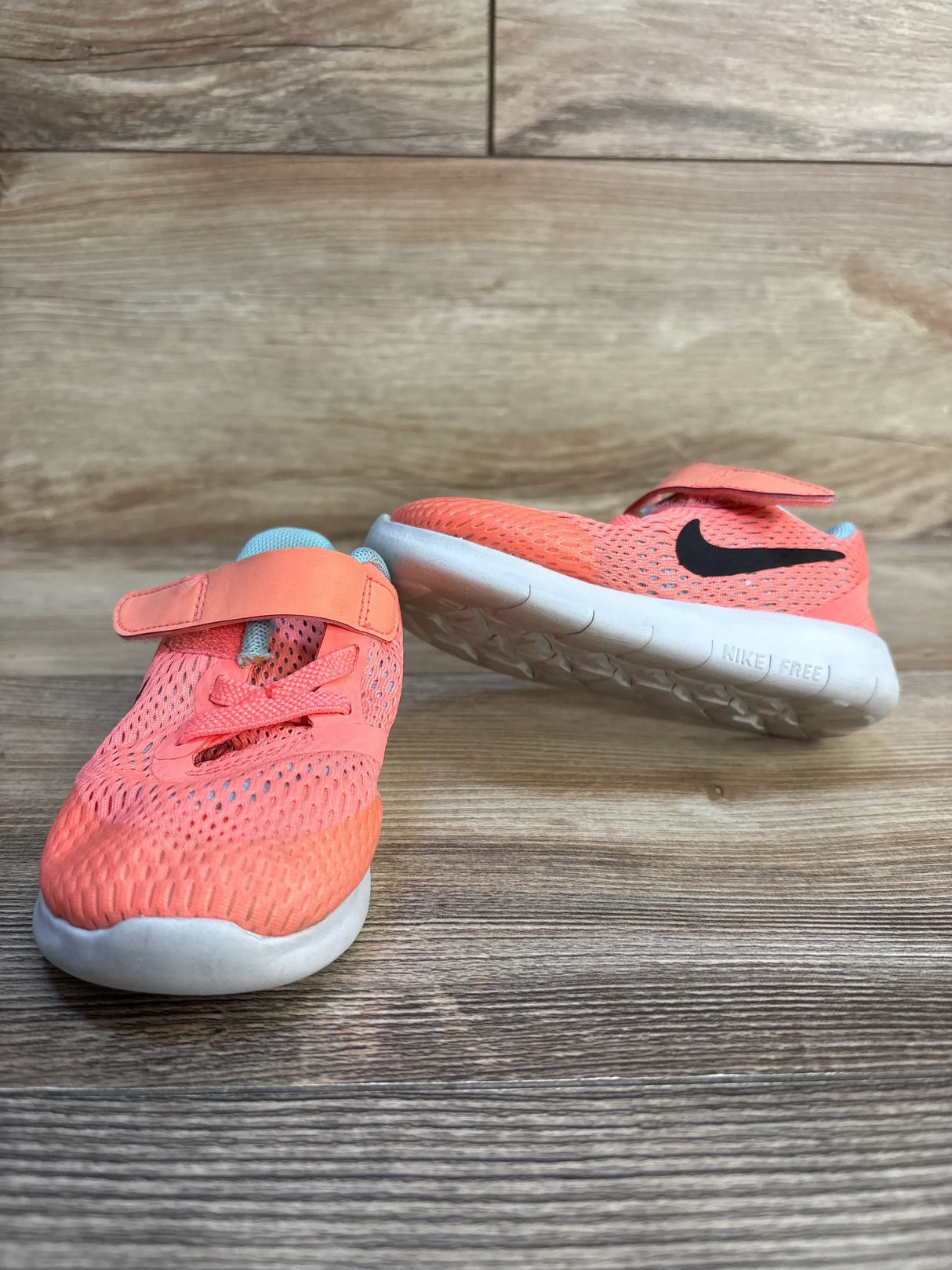 Coral pink kids Nike sneakers with white soles and Velcro straps on wood floor
