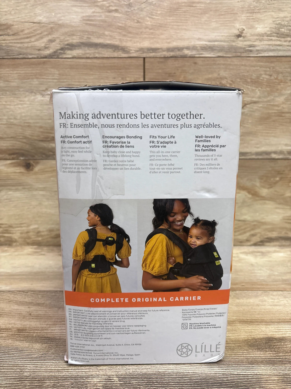 Front view of LILLEbaby Complete Original carrier box showing headline “Making adventures better together” and photos of a woman wearing the carrier against a wood background
