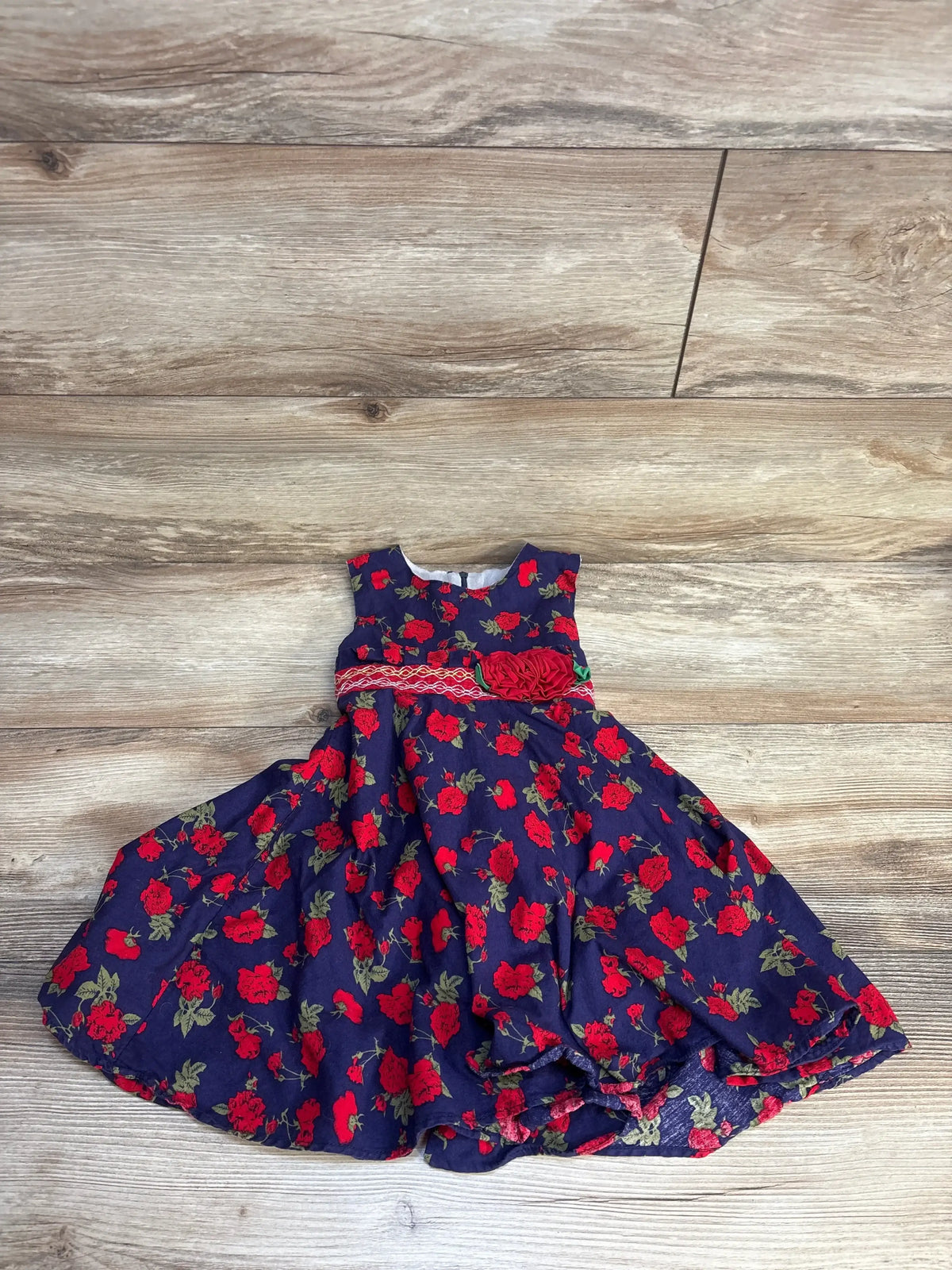 Navy blue toddler dress with red rose print and floral waist accent, laid on wood floor