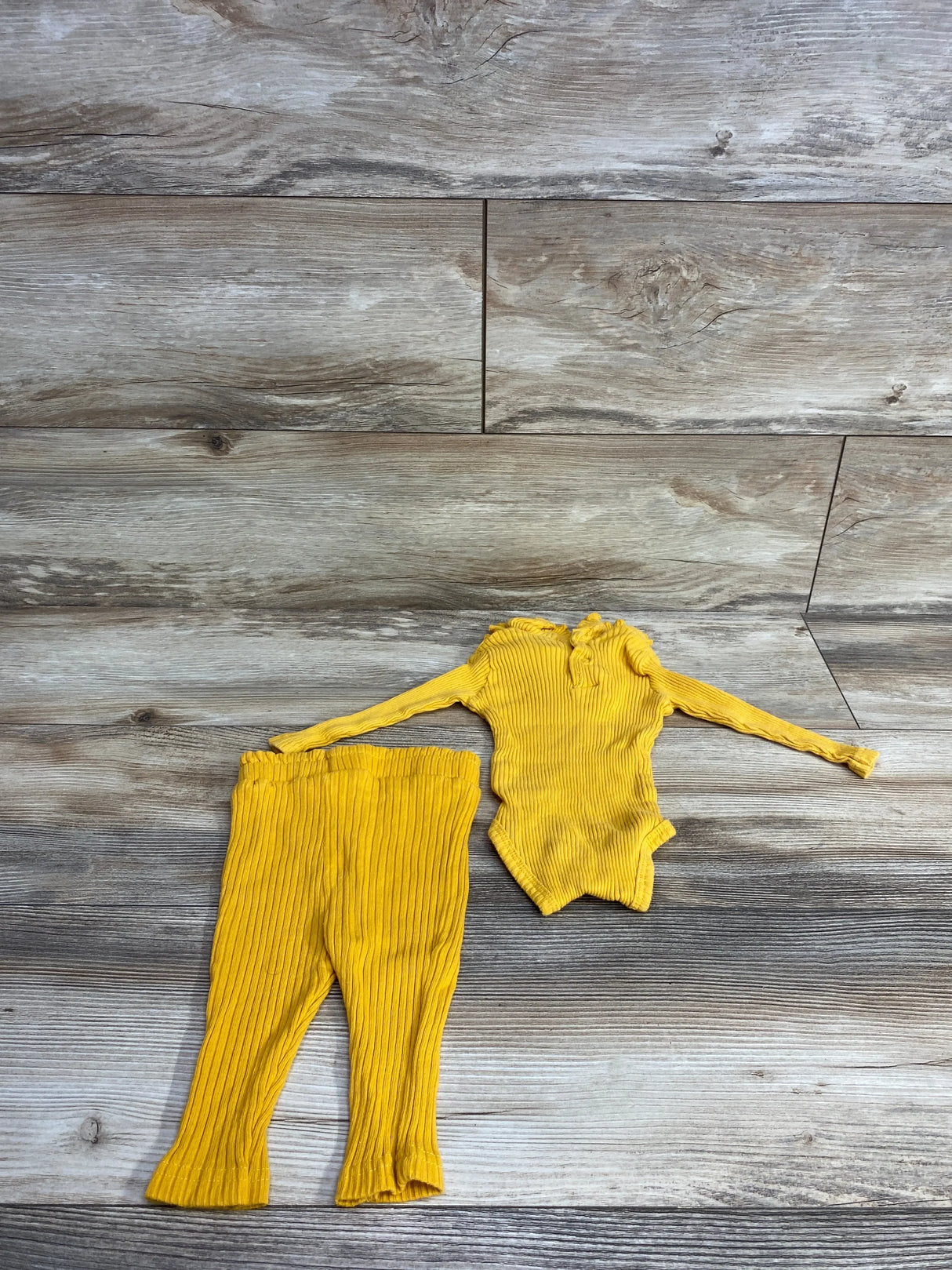 Yellow ribbed long sleeve baby bodysuit and matching pants set on wooden floor