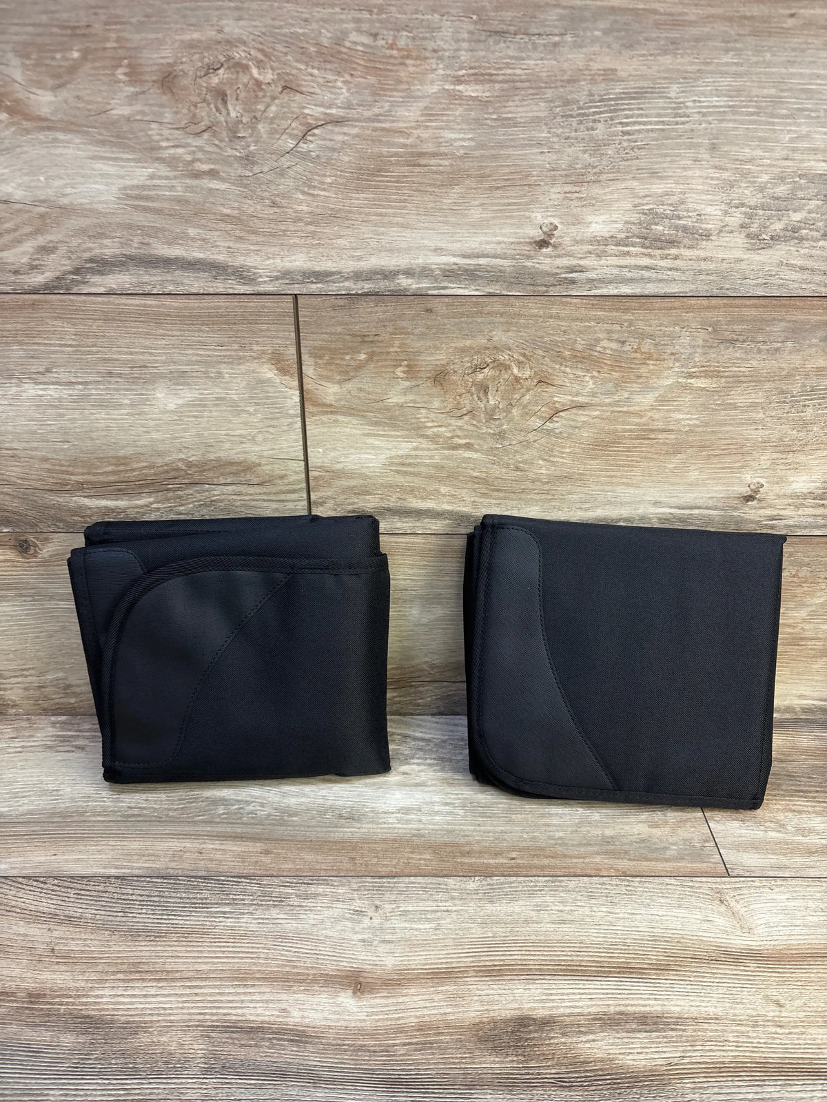 Top view of two black Bacgnyer car seat protectors showing contoured panels on a wood-look floor