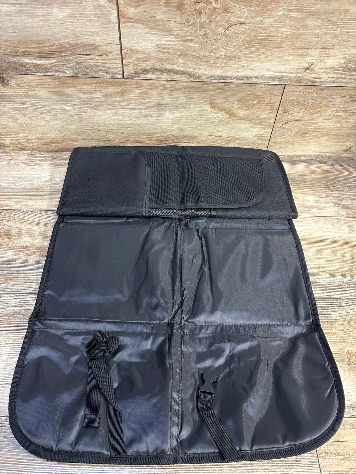 Top view of one black Bacgnyer car seat protector from a 2pk set with mesh pockets and fastening straps on wood flooring