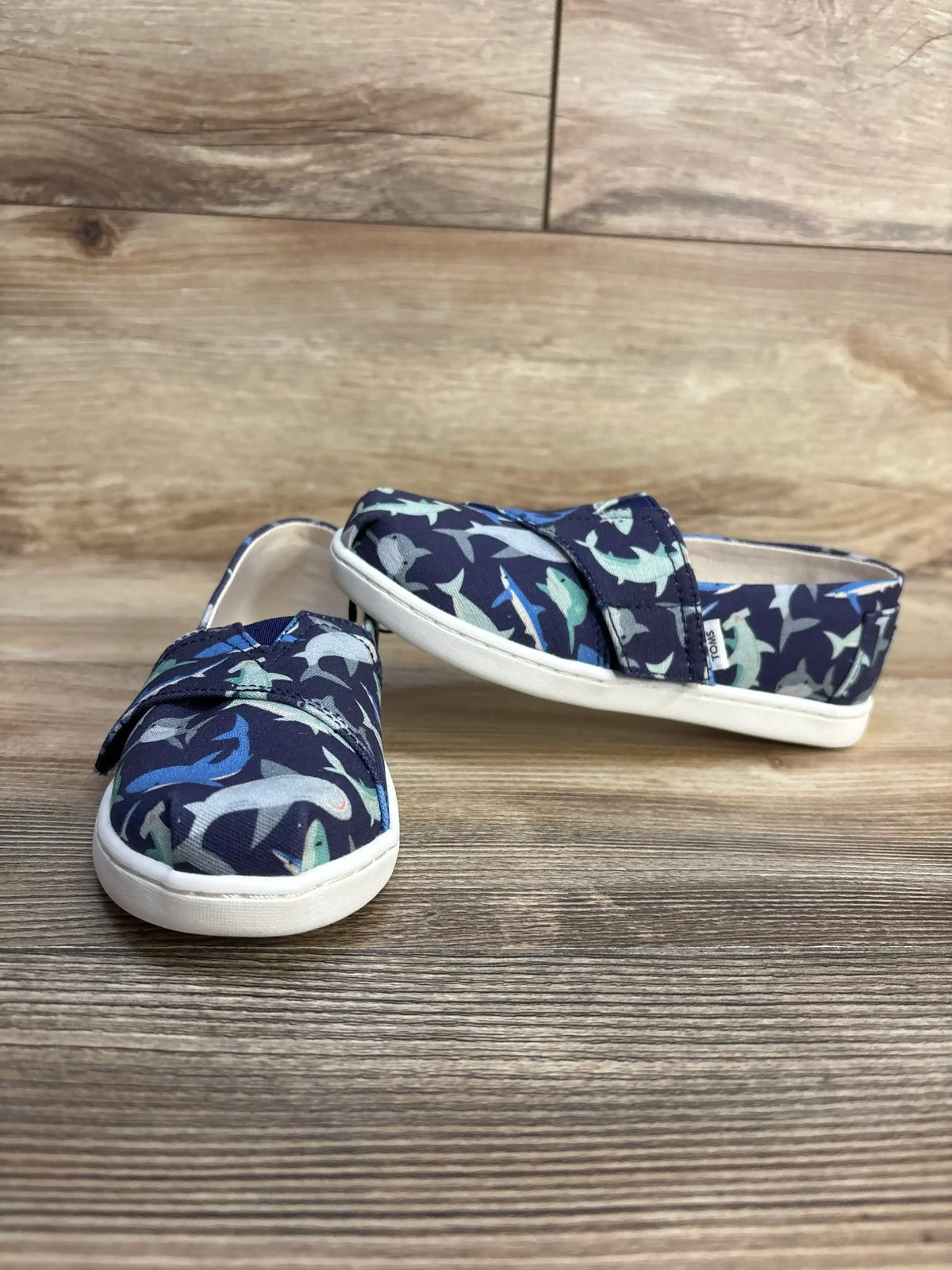 TOMS kids' slip-on shoes with shark print, navy blue canvas, white sole, on wood floor