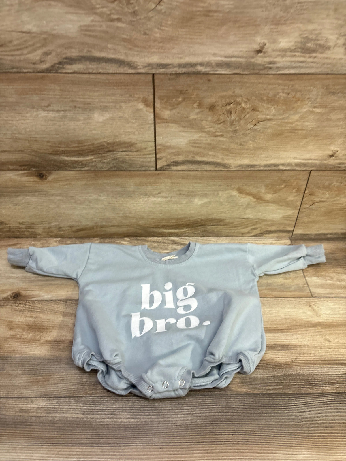 Front view of blue Big Bro sweatshirt bubble romper in size 6 to 9 months showcasing white big bro lettering on a wood floor