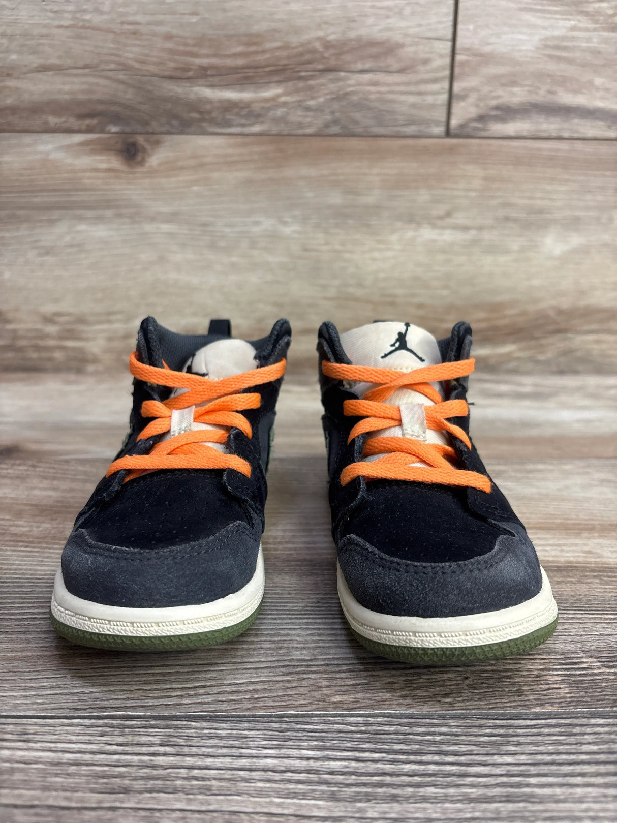 Toddler black sneakers with orange laces and white soles on wooden floor