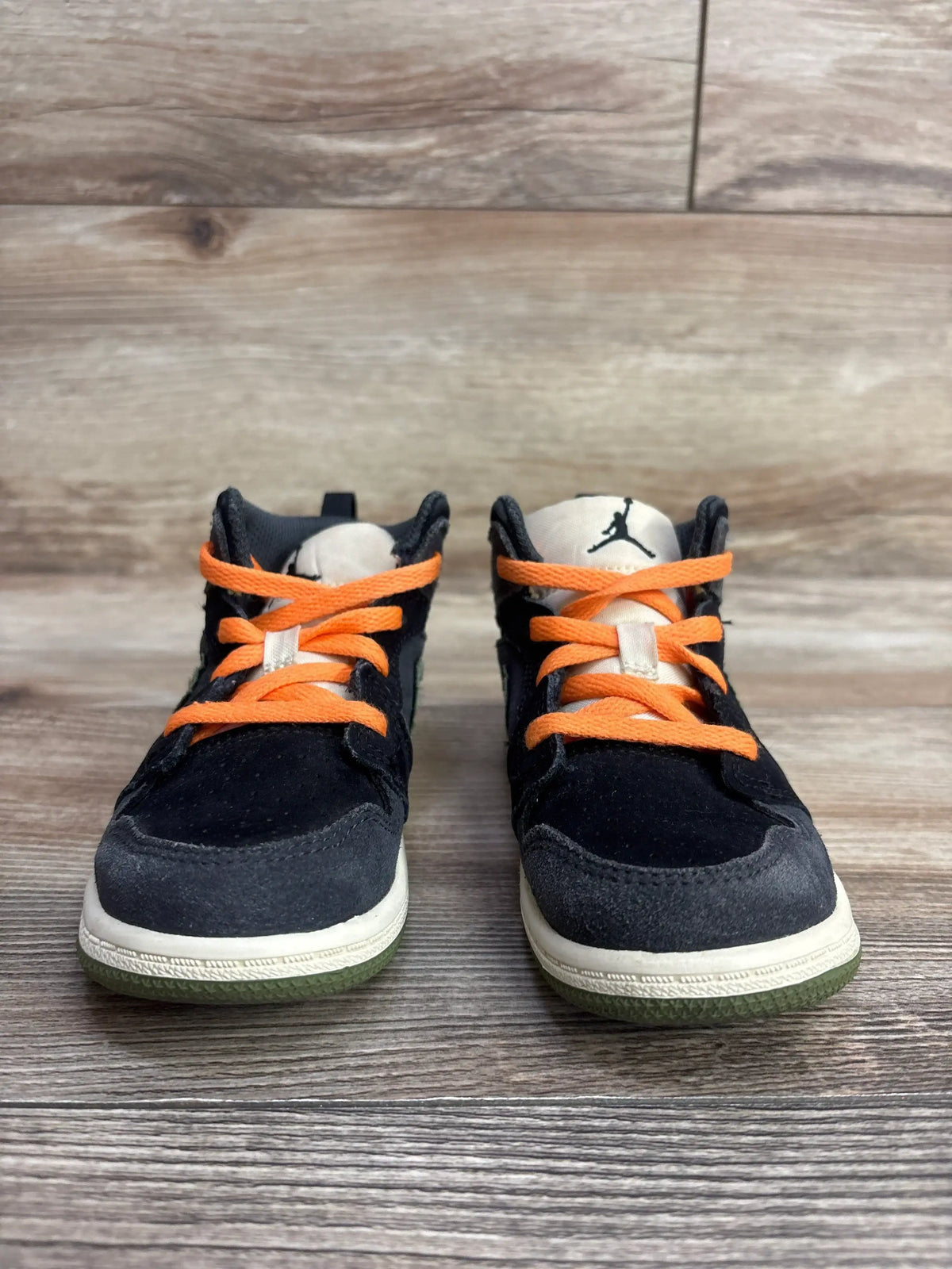 Toddler black sneakers with orange laces and white soles on wooden floor