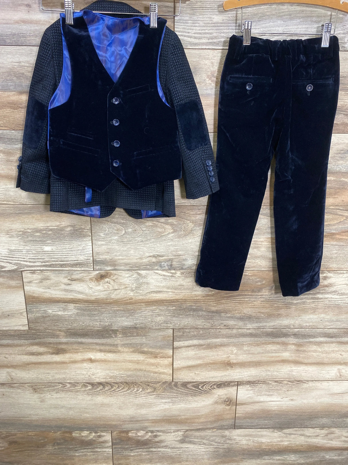 Front view of boys navy velvet three-piece suit (blazer, vest, pants) showing blue satin lining on wooden background