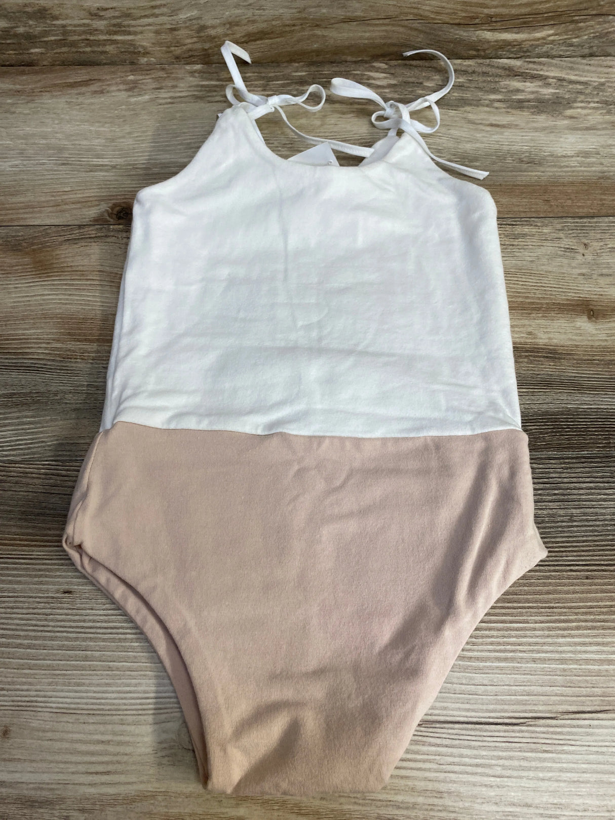 Flat lay of girls' two-tone leotard size 4-5T showcasing white halter top with tie shoulder straps and blush bottom on wood background