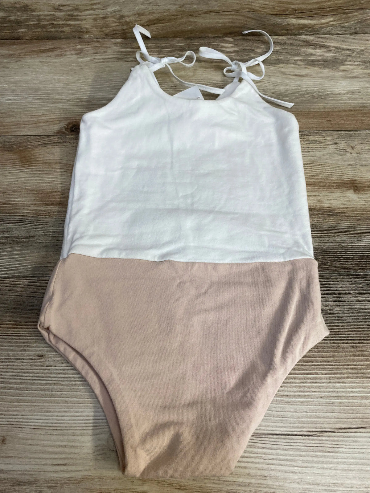 Flat lay of girls' two-tone leotard size 4-5T showcasing white halter top with tie shoulder straps and blush bottom on wood background