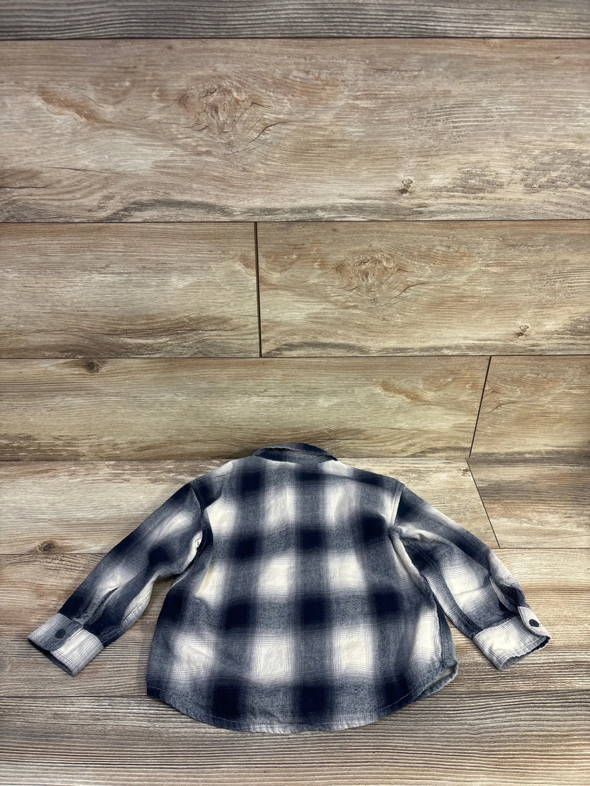 H&M button-up flannel shirt in blue and white plaid for toddlers, laid flat on a wood background.