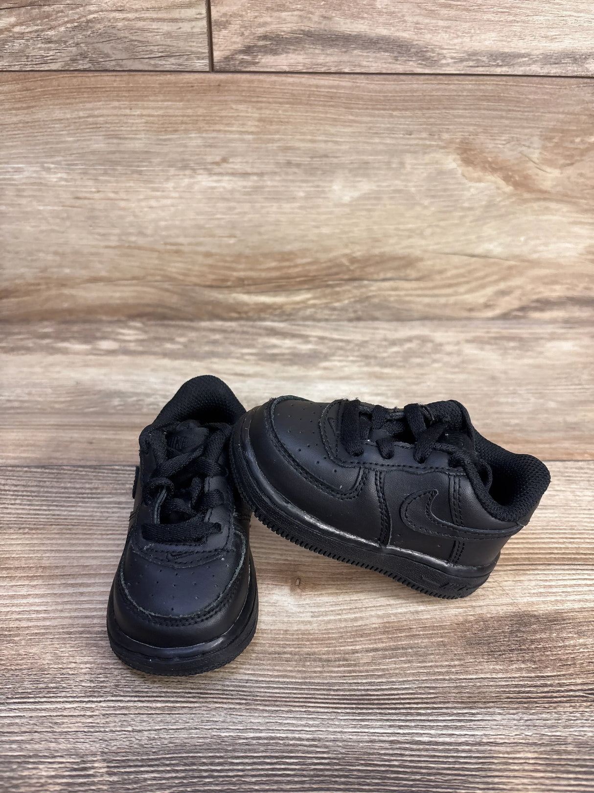 Side view of Nike Air Force 1 06 TD Triple Black Sneakers sz 4c showcasing all-black leather upper with tonal swoosh and black laces on wood plank floor