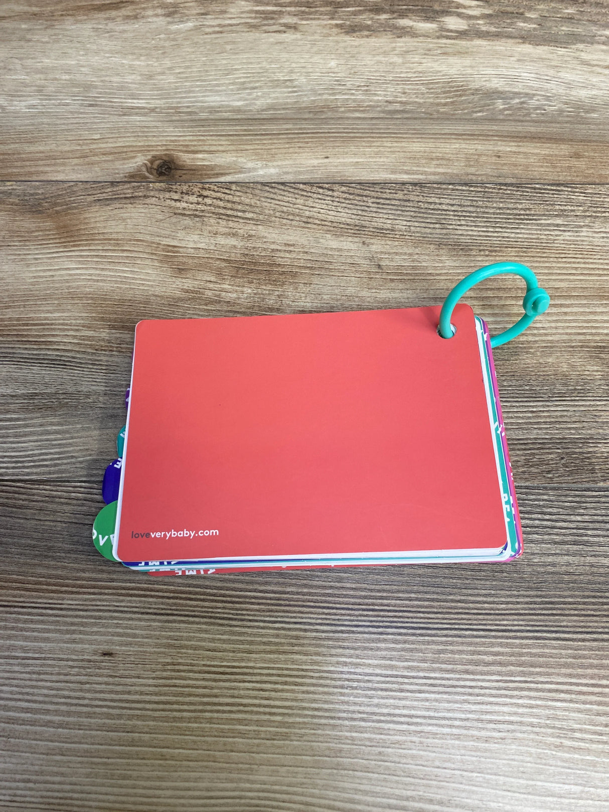 Red baby flashcards with colored tabs and blue ring on wooden surface, loveverybaby.com logo