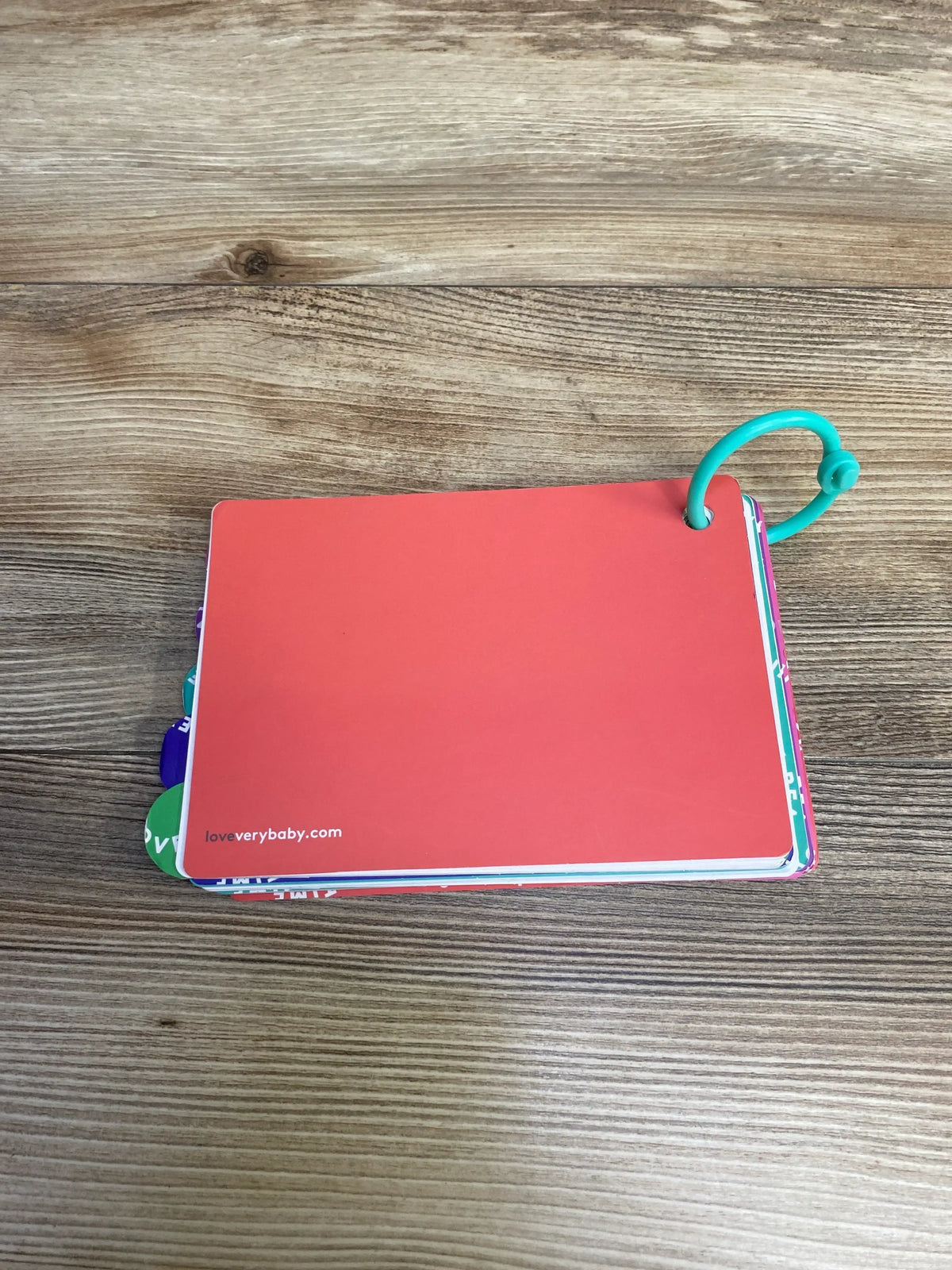 Top view of Lovevery The Senser Play Guide flashcards showing red cover, colored tabbed cards and turquoise plastic ring on a wood surface