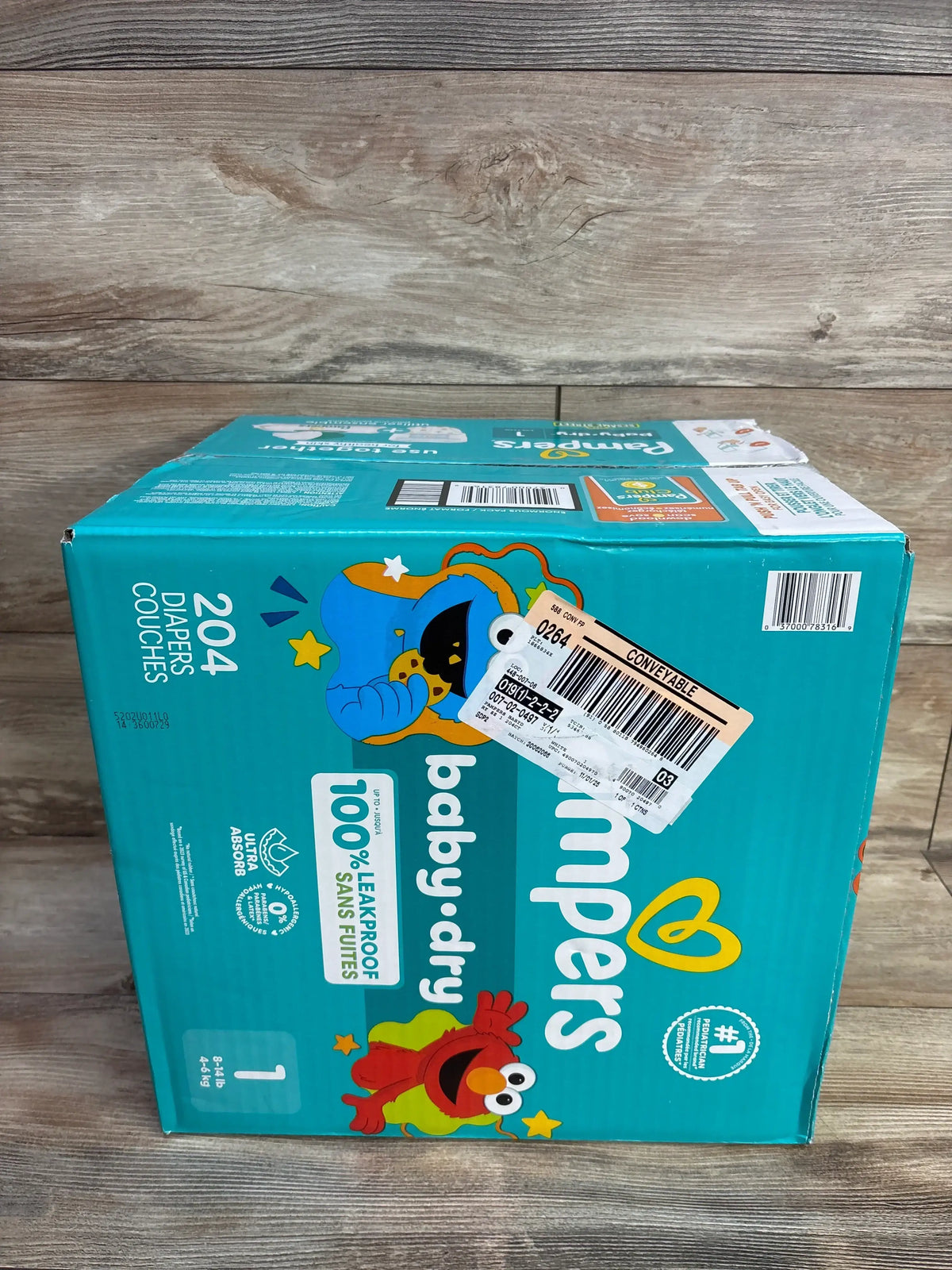 Three-quarter view of NEW Box of Pampers Baby Dry Diapers Pack 204ct Size 1 showcasing teal box with Sesame Street characters and 100 percent leakproof label on wood plank floor