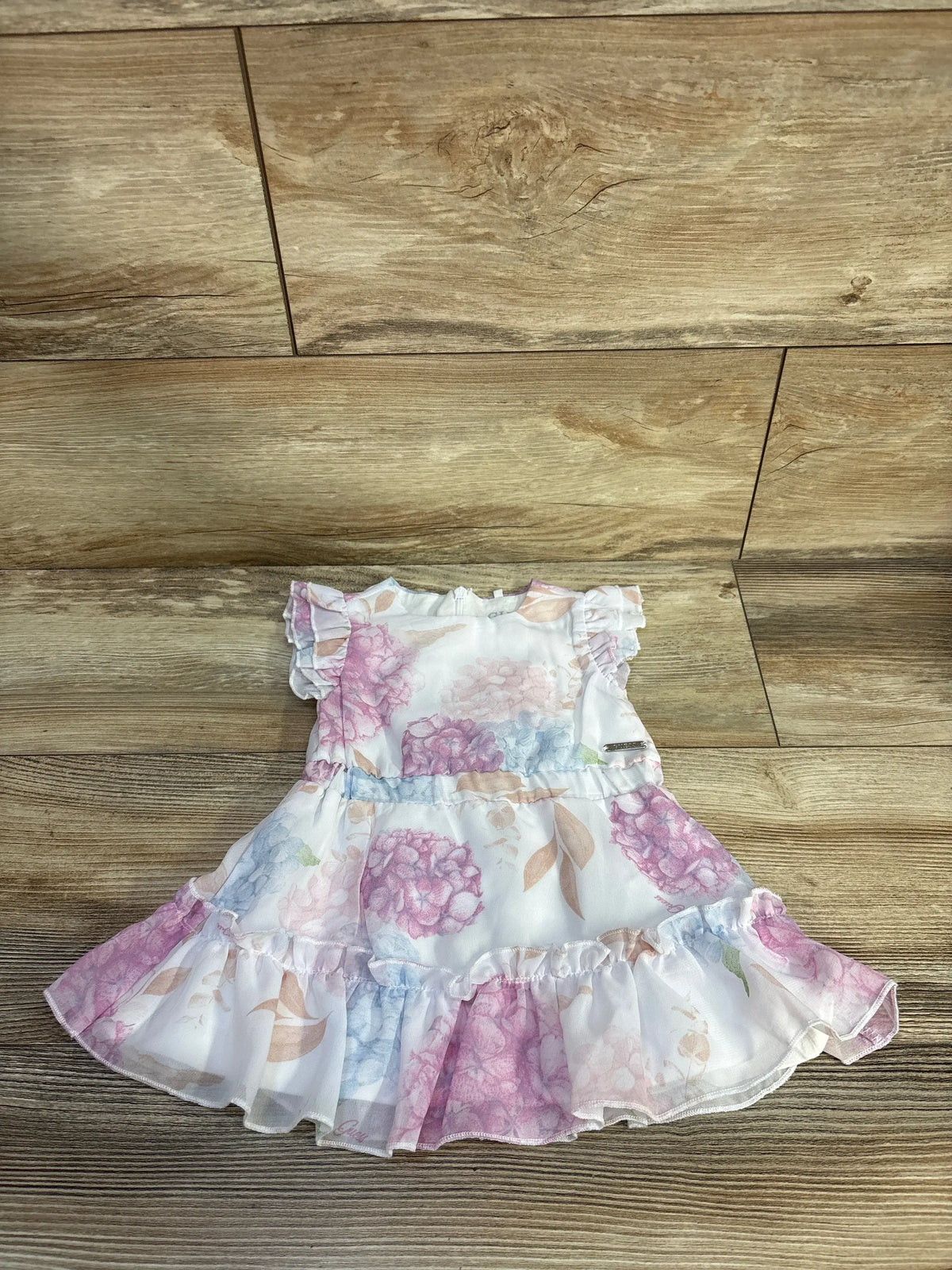 Front view of Guess floral tulle dress showcasing pastel floral print, ruffled sleeves and skirt on a wood floor