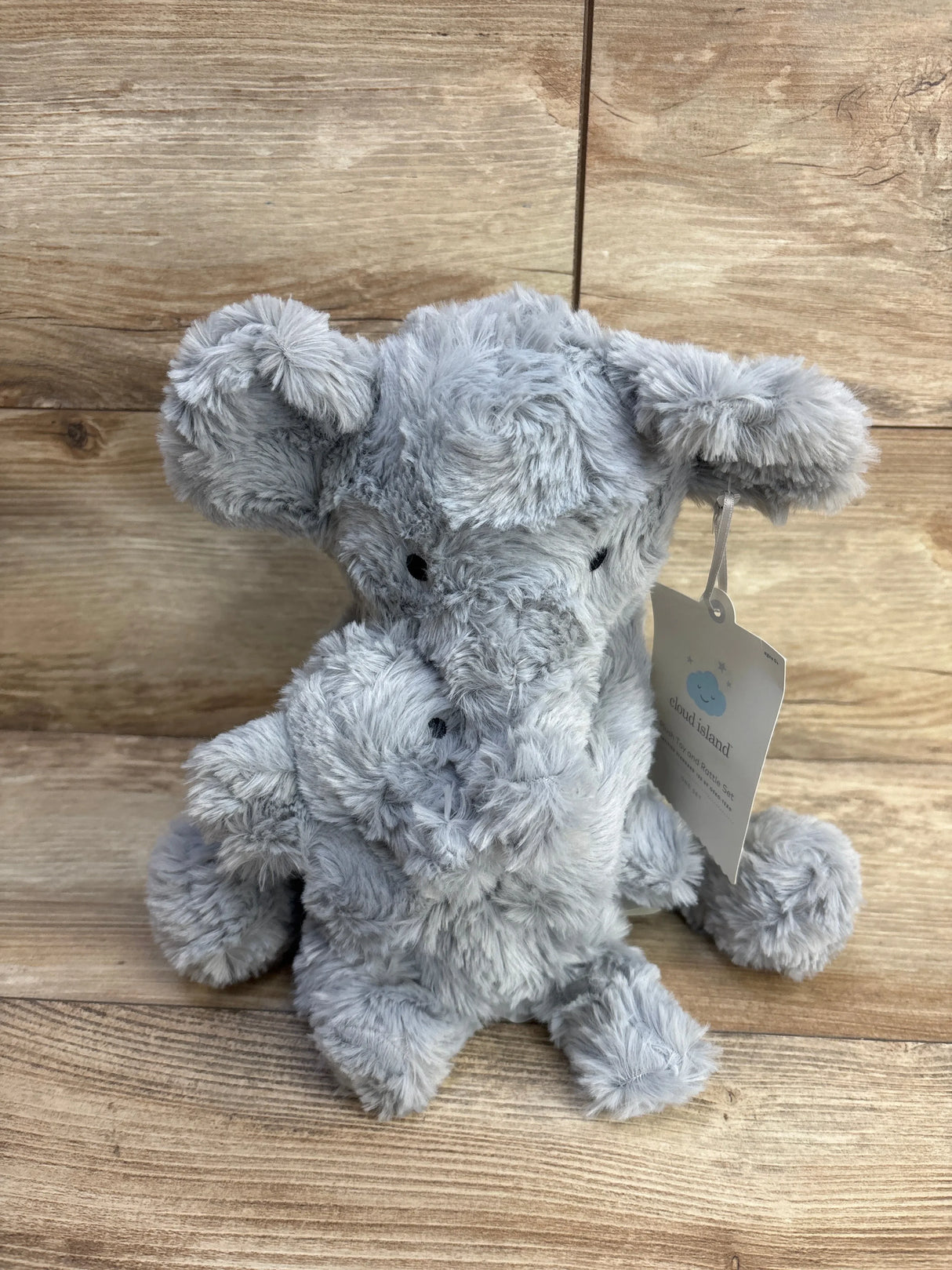 Front view of Cloud Island grey elephant plush holding a mini elephant, showing soft fur and black eyes on wood background