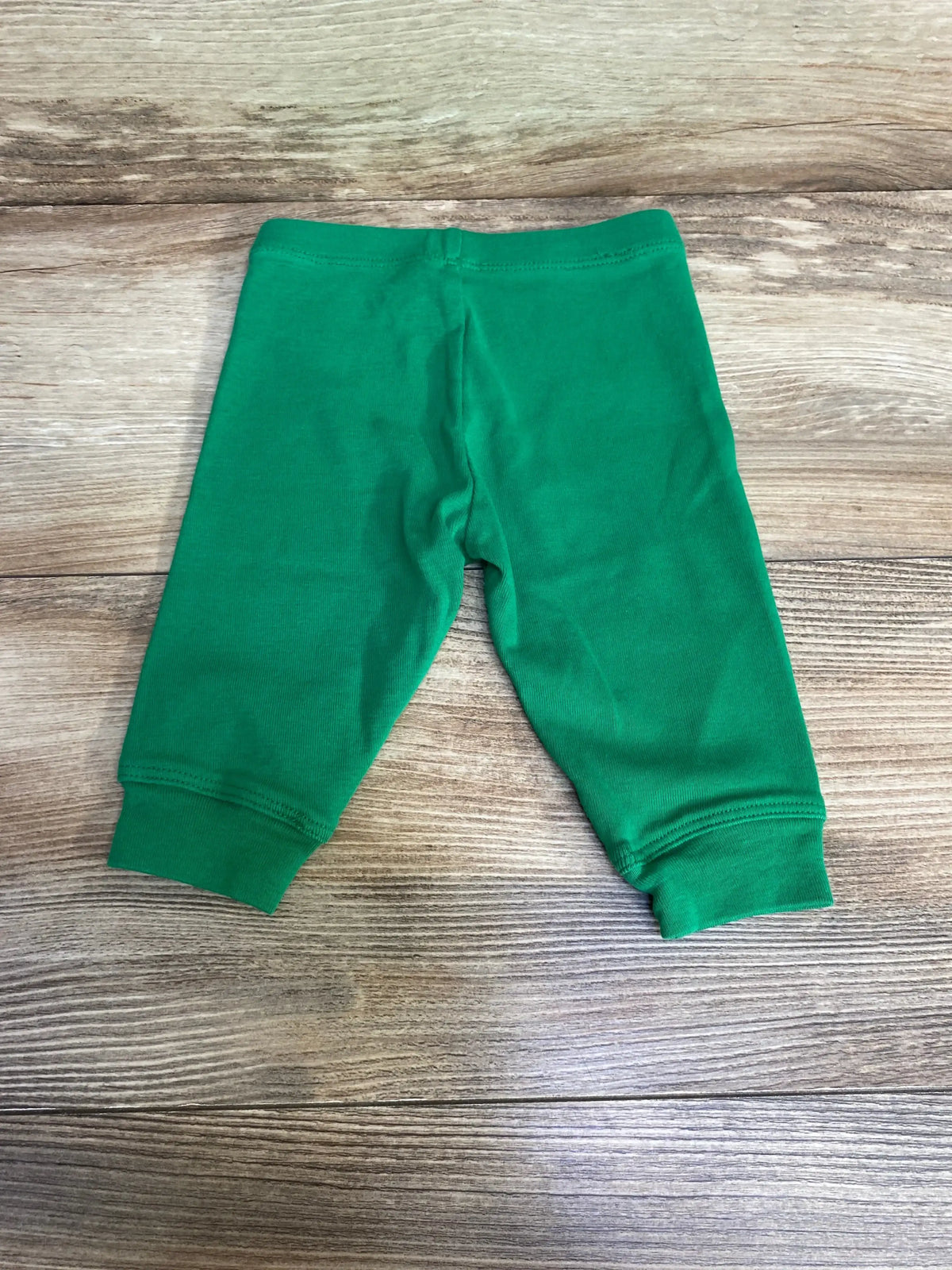 Flat lay of green newborn pull-on baby pants showcasing elastic waistband and ribbed ankle cuffs with wood plank background