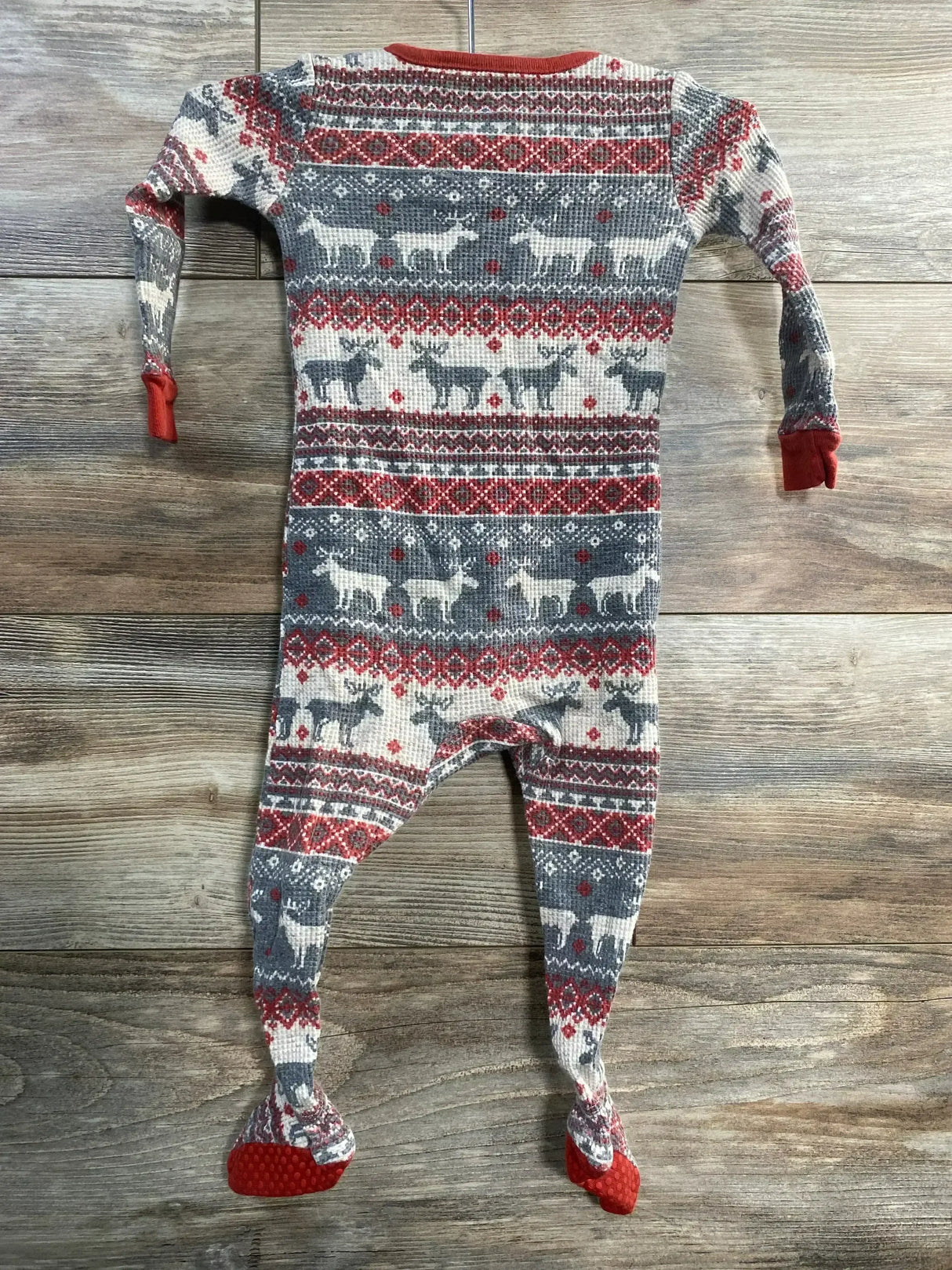 Flat-lay of grey Fair Isle footed sleeper showing reindeer pattern, red trim, fold-over cuffs and grippy soles on wood