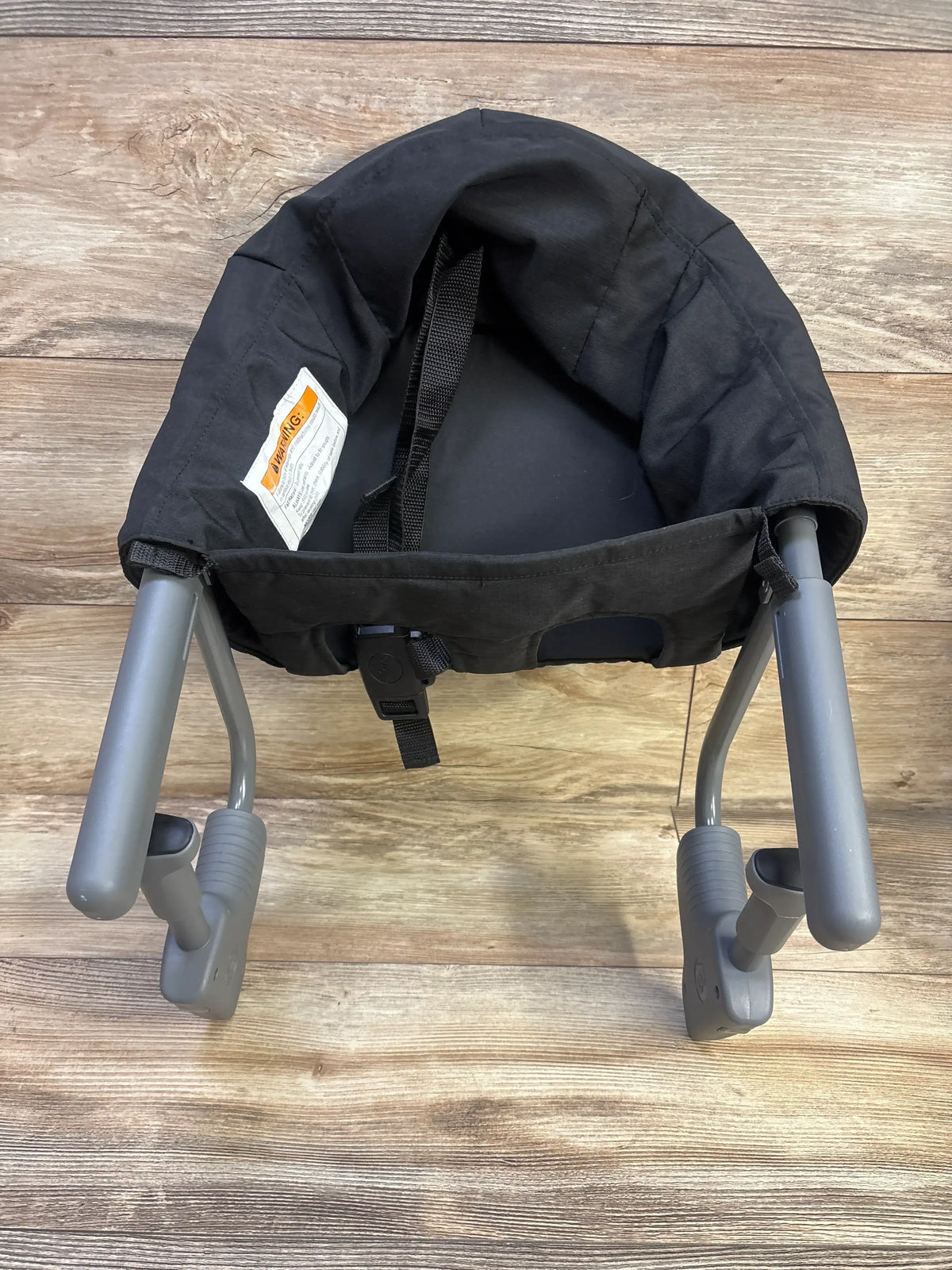 Front view of Chicco FastLock Hook-On Chair in black with safety harness and gray support clamps on a wood floor